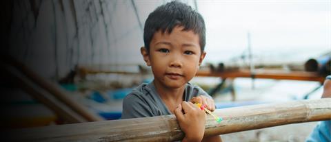a young boy leans on wooden fence looking at the camera