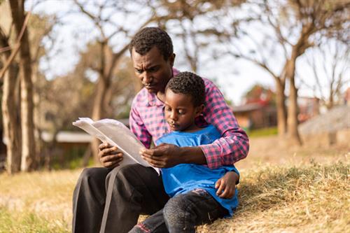 A man reads a Bible with a child outside