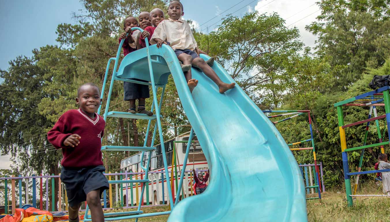 Boys sliding down a slide on a playground in Kenya