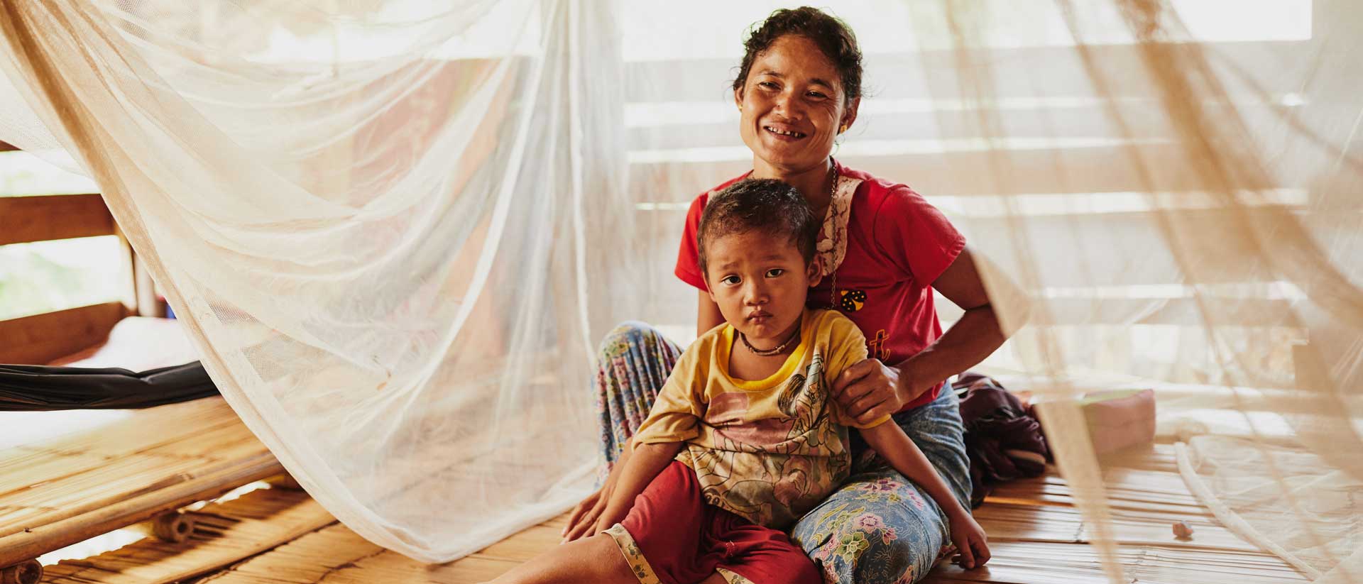 A mom sits with her son under a mosquito net