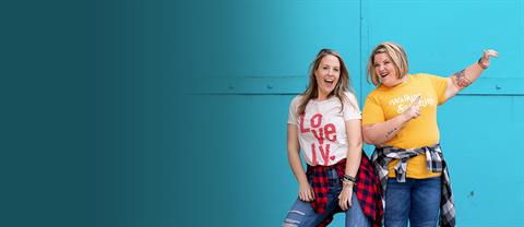 Two woman stand near a teal wall laughing