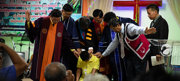 Several church leaders pray over a boy kneeling on the floor.