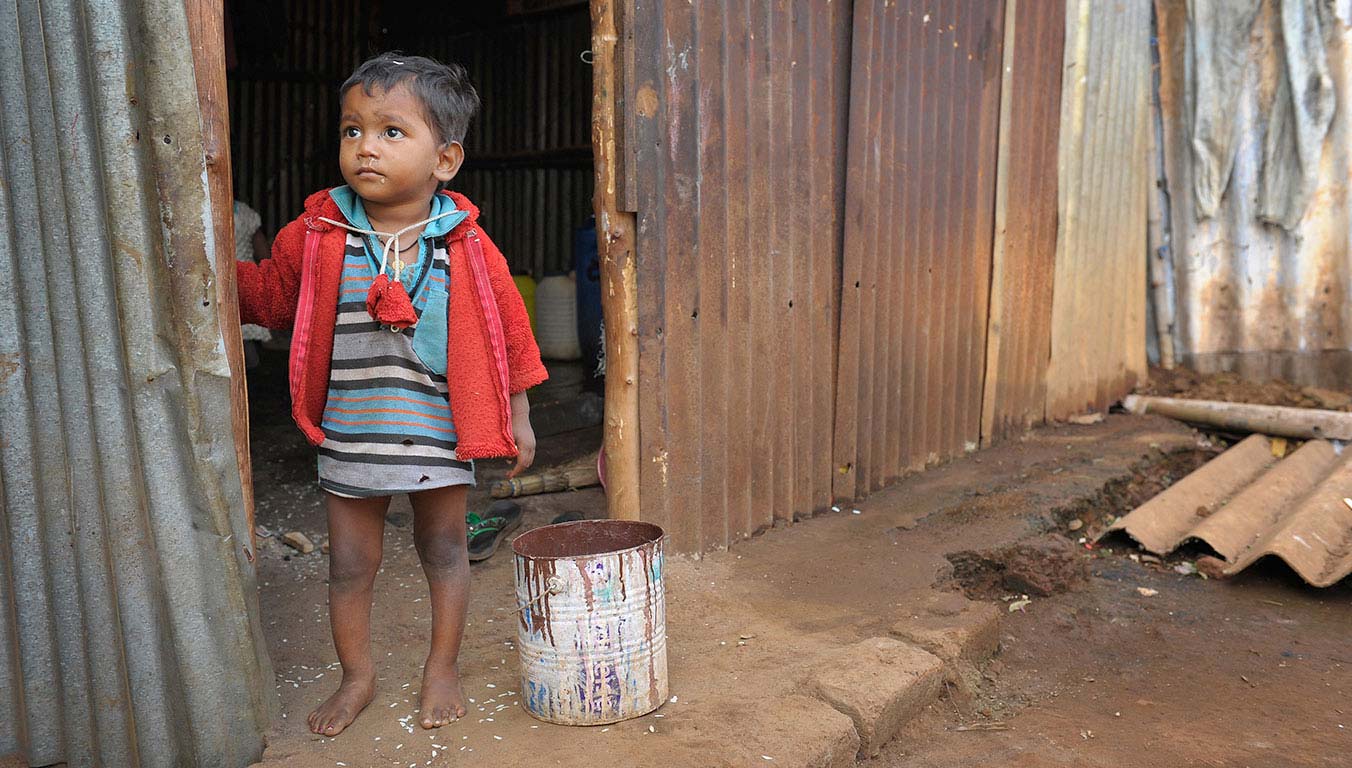 A young boy standing barefoot outside his home