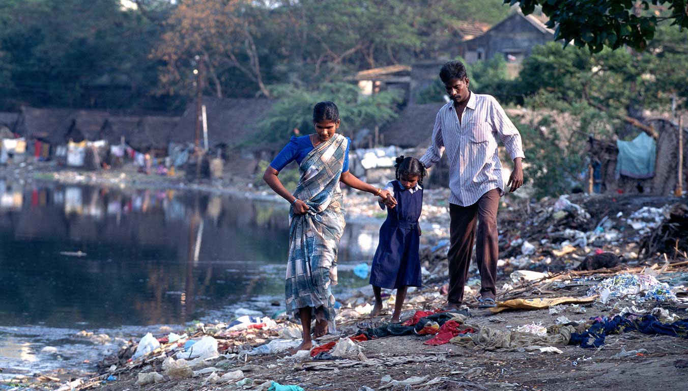 A father, mother and their child walk through a trash pile