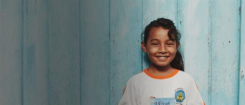 A smiling girl stands in front of a light blue wall