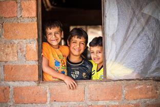 Three boys standing close together smiling from a window