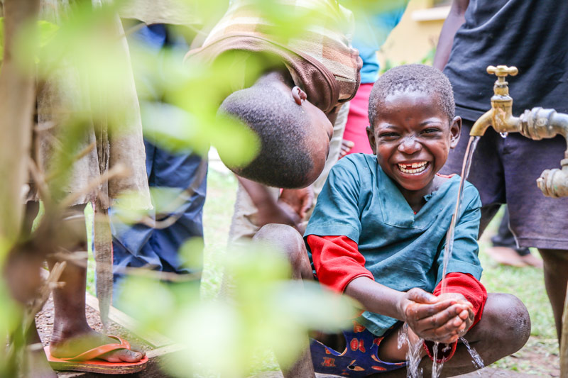 A boy smiles and washes his hands with clean water