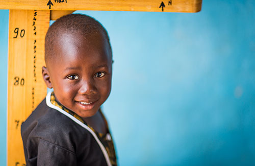 a smiling boy stands next to a height measurement chart