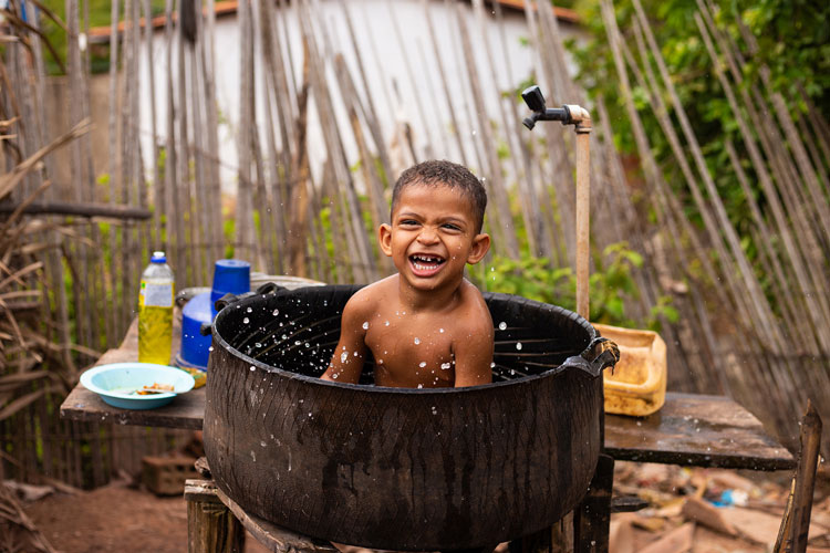 A young boy laughs while bathing in a large bucket tub