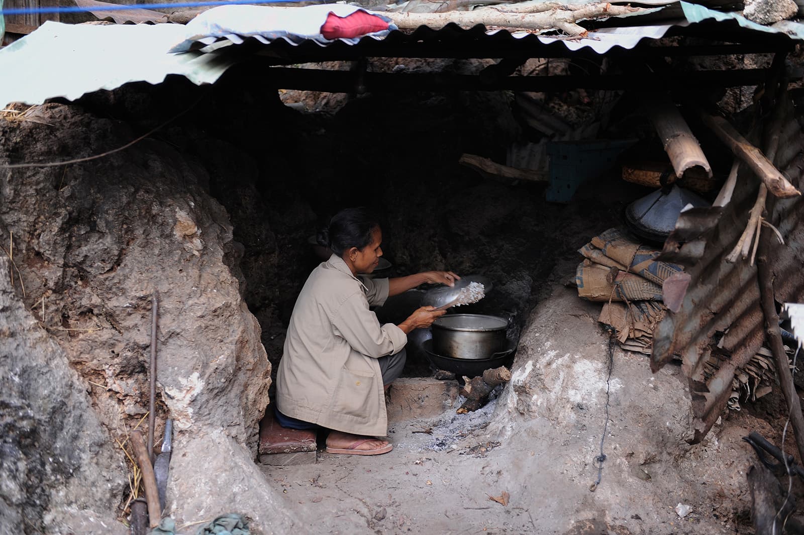 Woman cooks over a fire in a below ground kitchen.