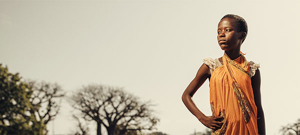 An African girl with a serious expression stands with a hand on her hip