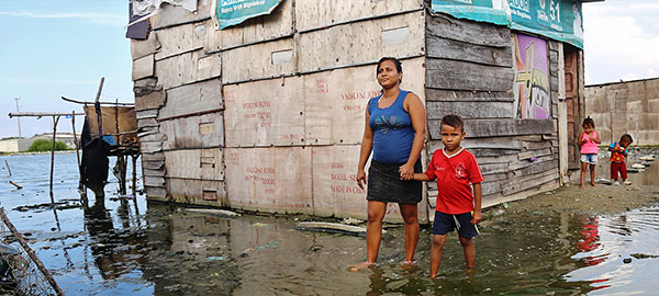 A woman and boy hold hands as they walk through ankle-deep water outside their home