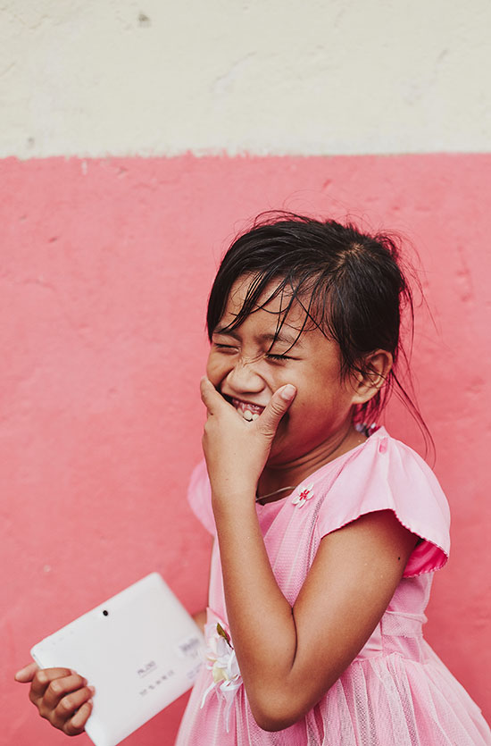 A girl in a pink dress covers her mouth with her hand as she laughs
