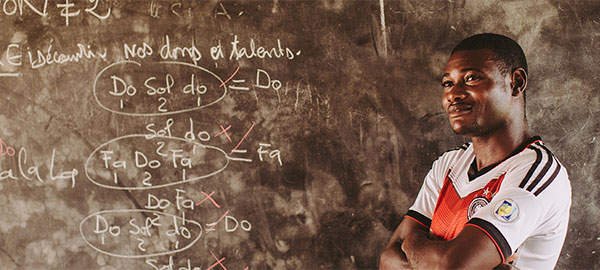 A male teacher stands in front of a chalkboard with his arms crossedd