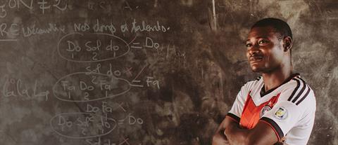 A male teacher stands in front of a chalkboard with his arms crossed