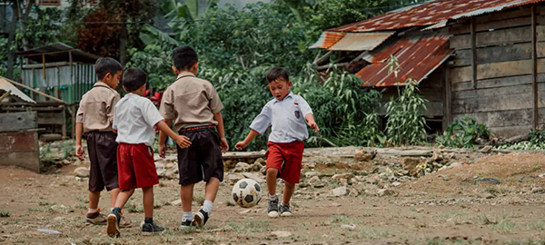 Boys race around the school playground kicking a soccer ball