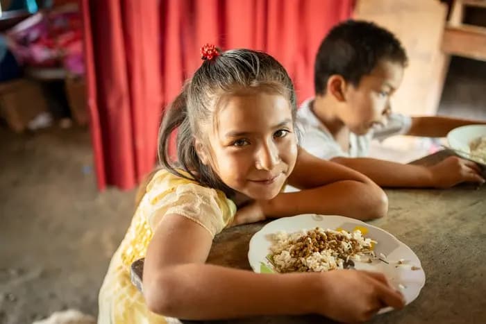 Janeth is at home eating rice and lentils that Vidalina prepared for her. Her brother Luis is sitting next to her.