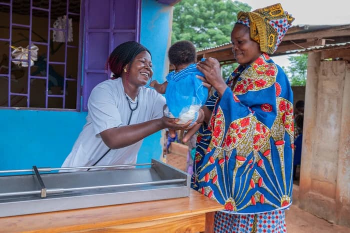 Sandra, a nurse, is handing Larissa back to her mother, Akouwa, after the baby's checkup.