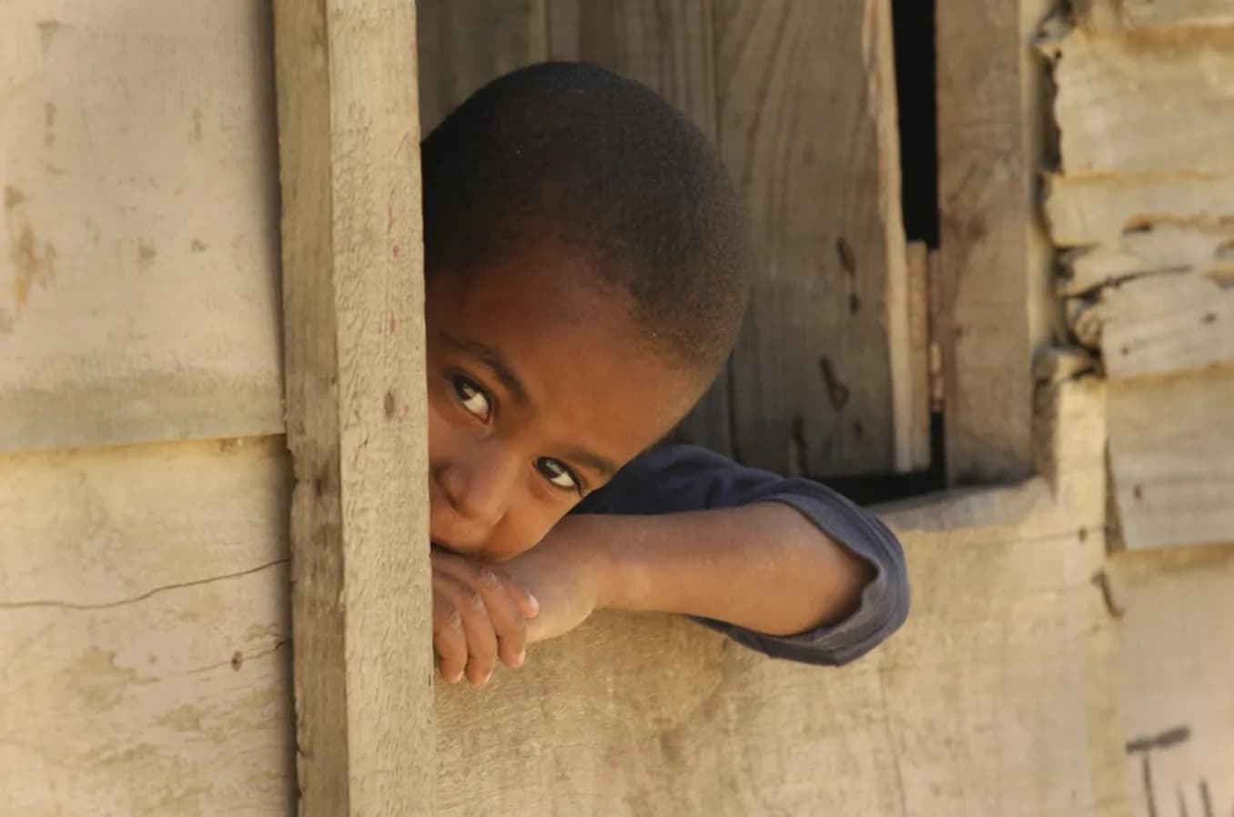 A boy looking out the window of his home.