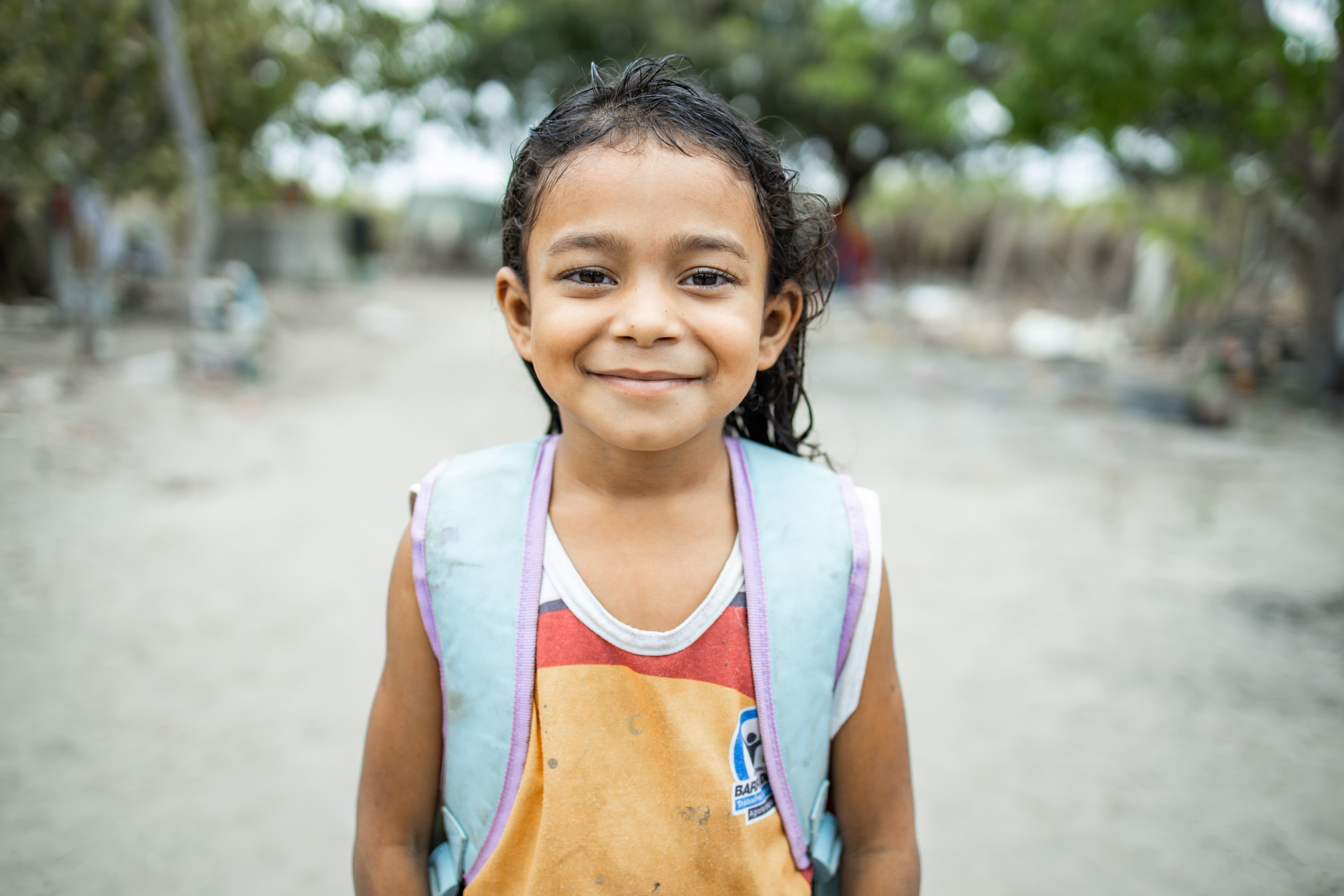 A young girl wearing a backpack smiles for the camera.