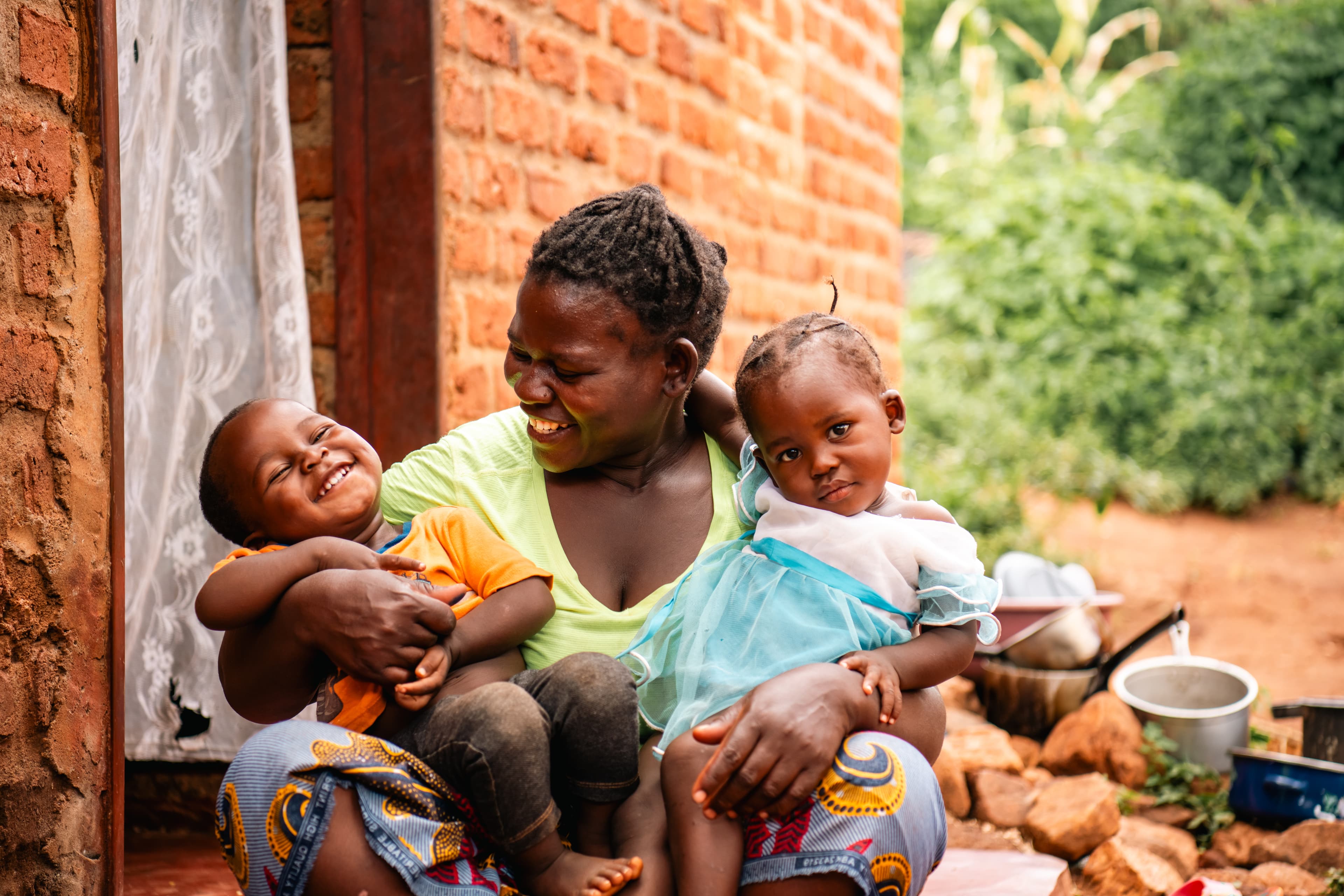 An African mom holds her two children outside a brick home.