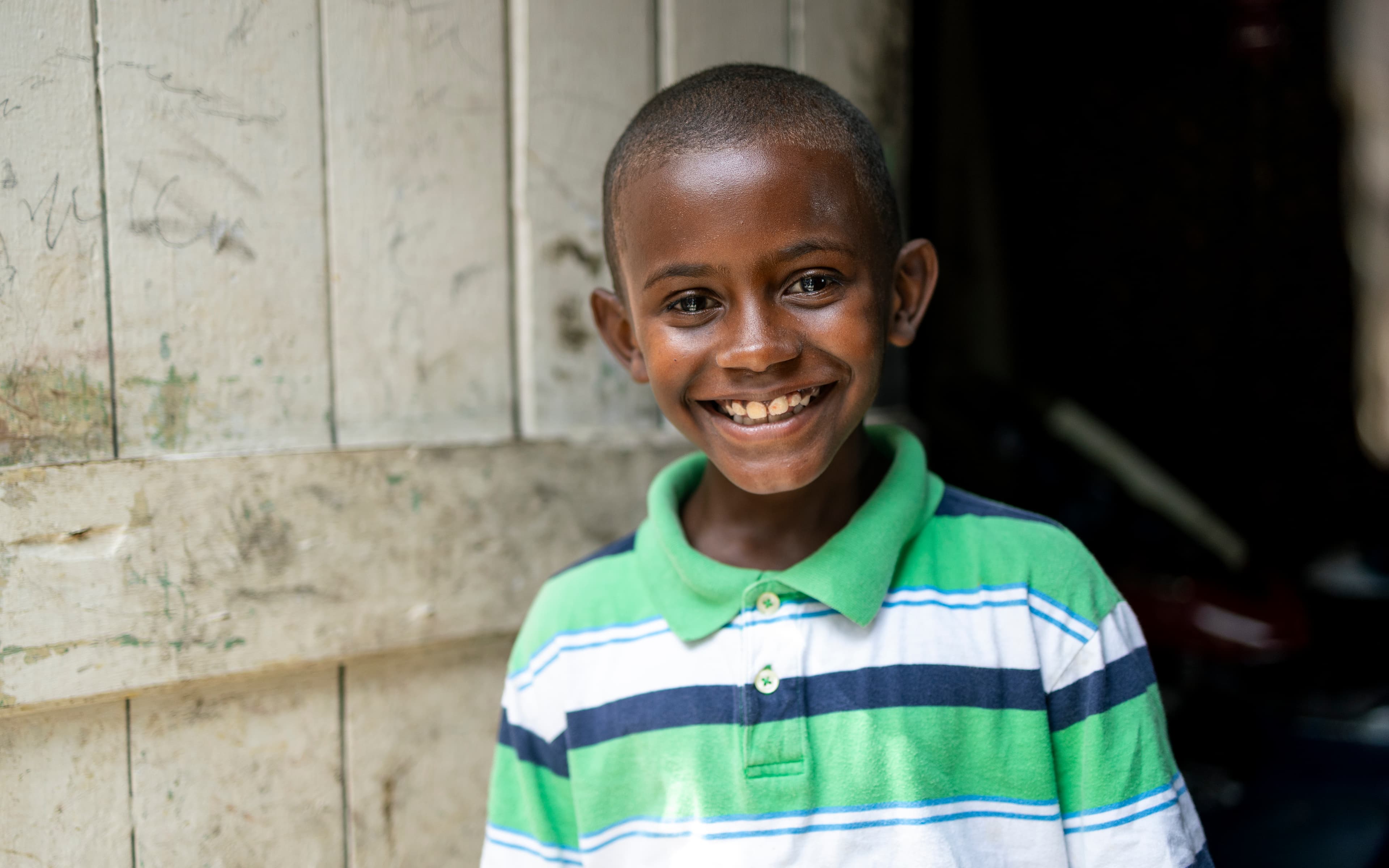 A young boy wearing a striped shirt smiles brightly for the camera.
