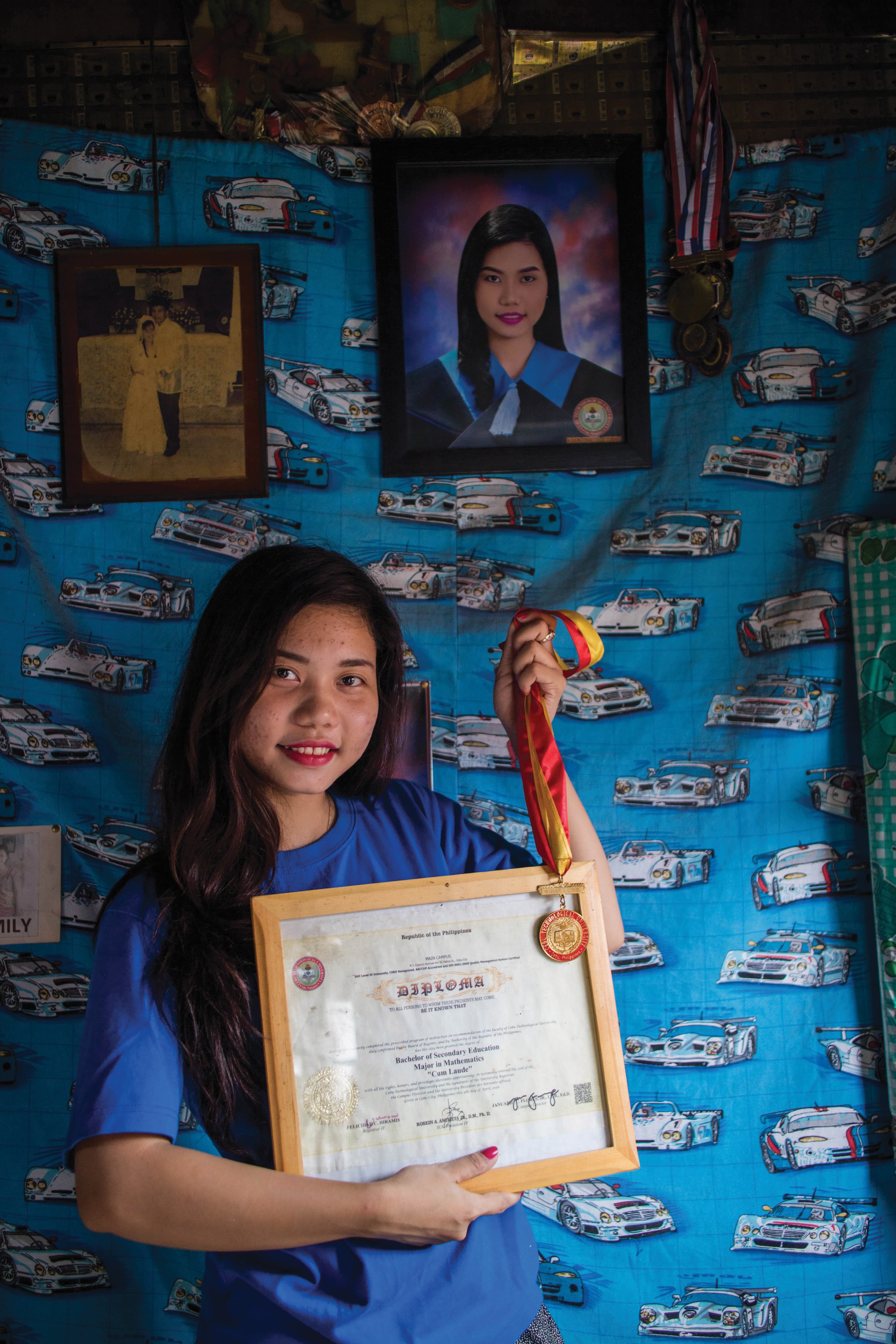 A young woman stands in a room holding up a diploma and medal.