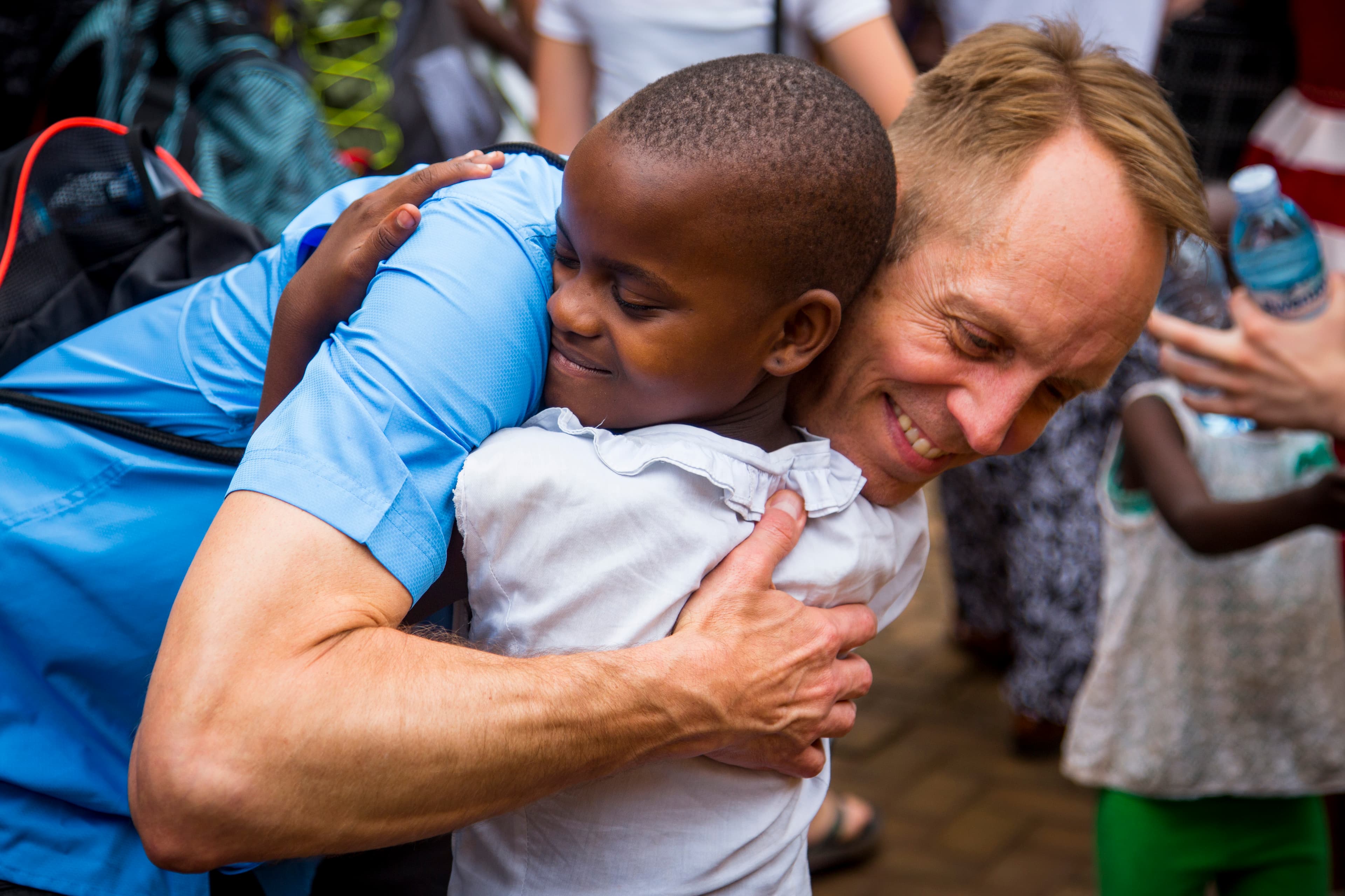 A man smiles and bends down to hug a young child.