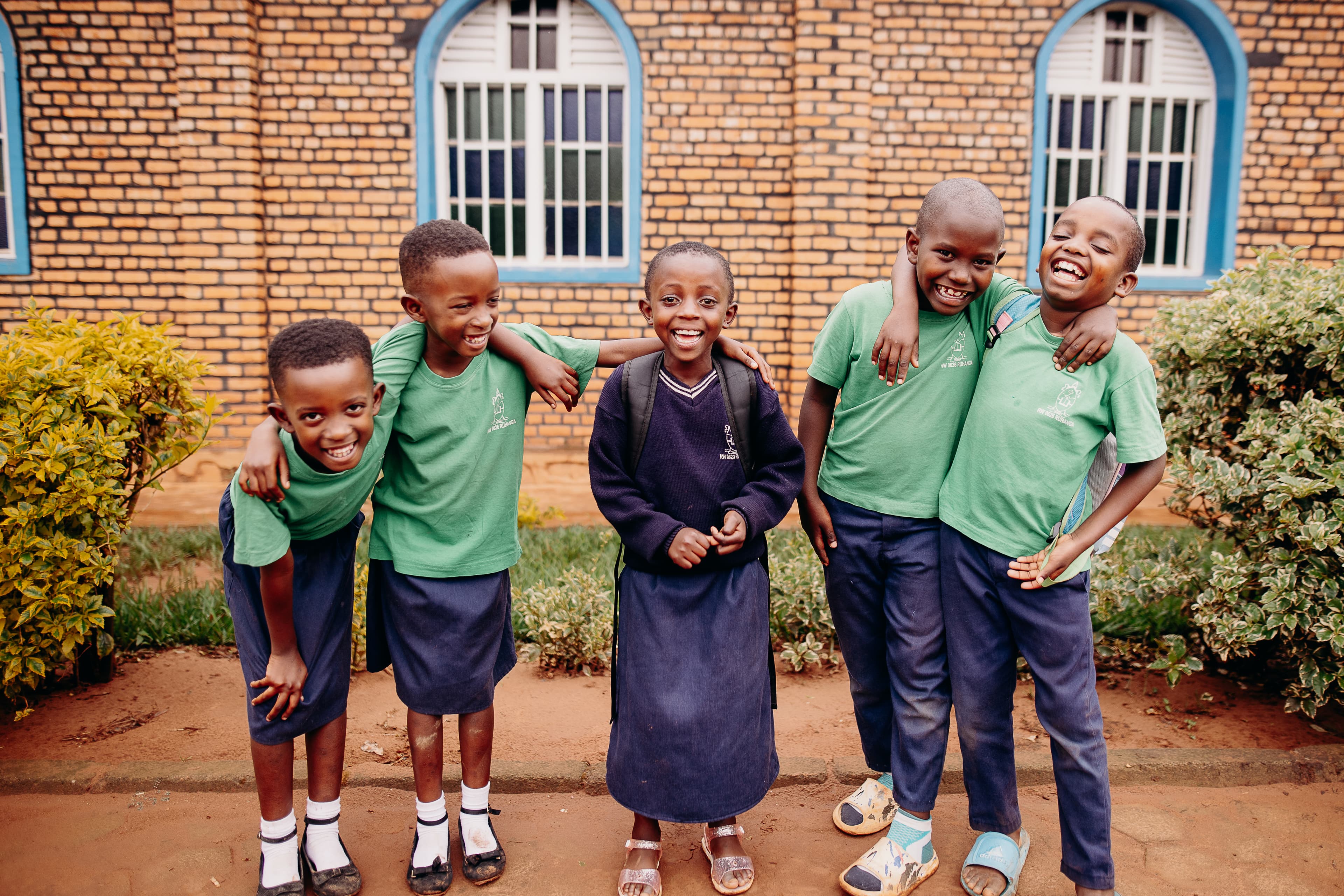 Rwandan school kids in uniforms smile and embrace each other.
