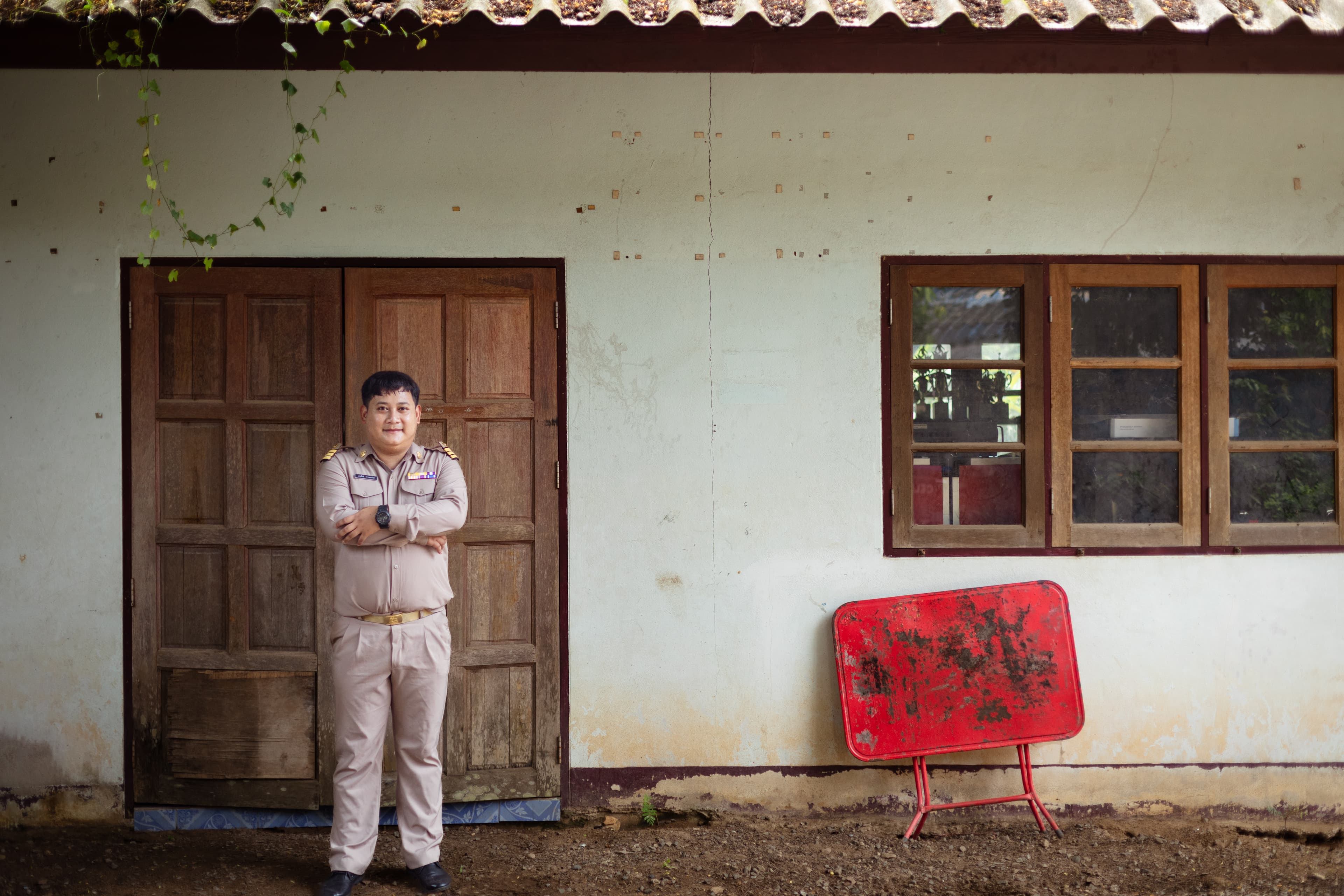A man in a uniform stands with his arms crossed in from of a building.