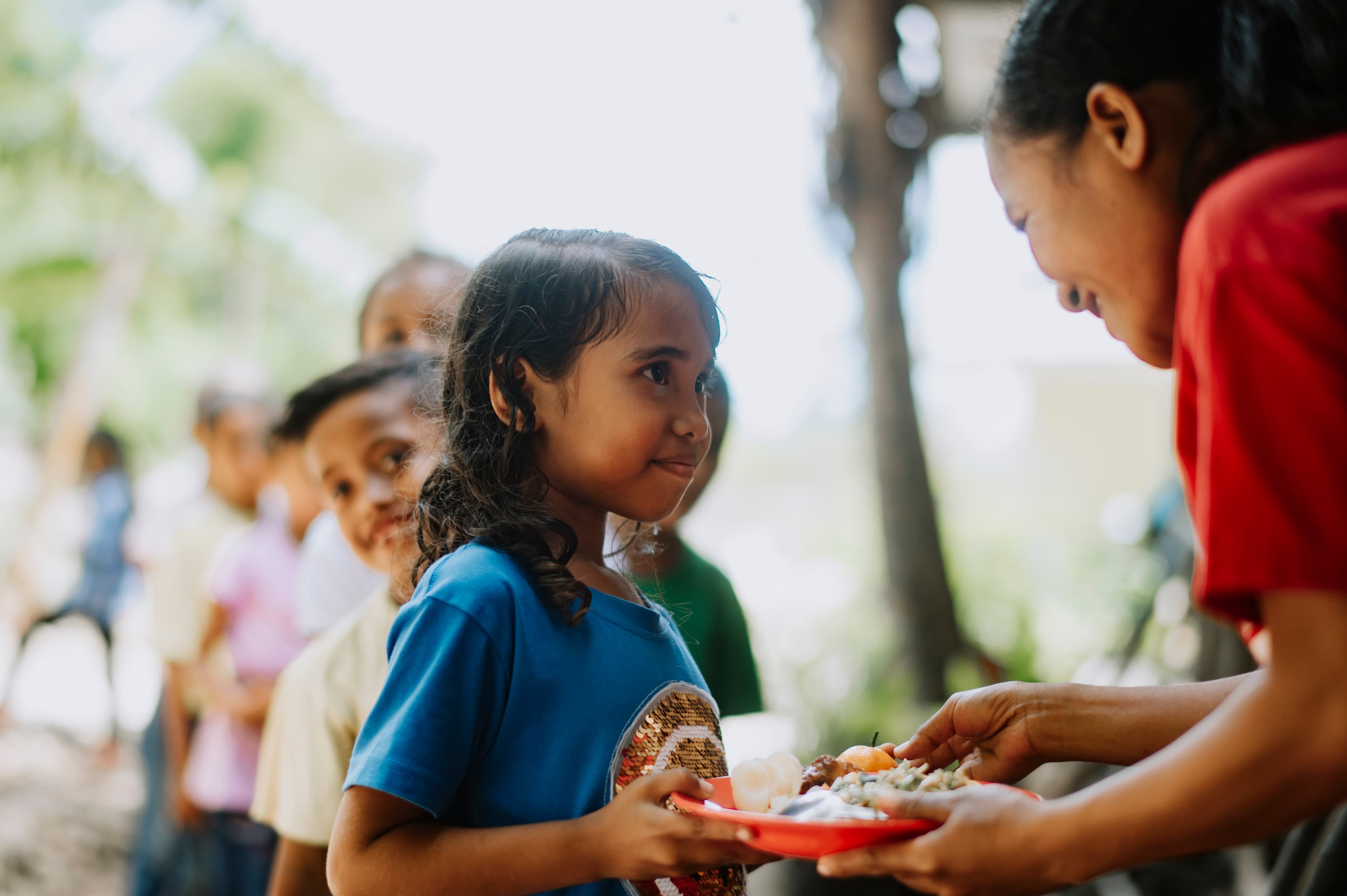A young girl is given a plate of food by an older woman.
