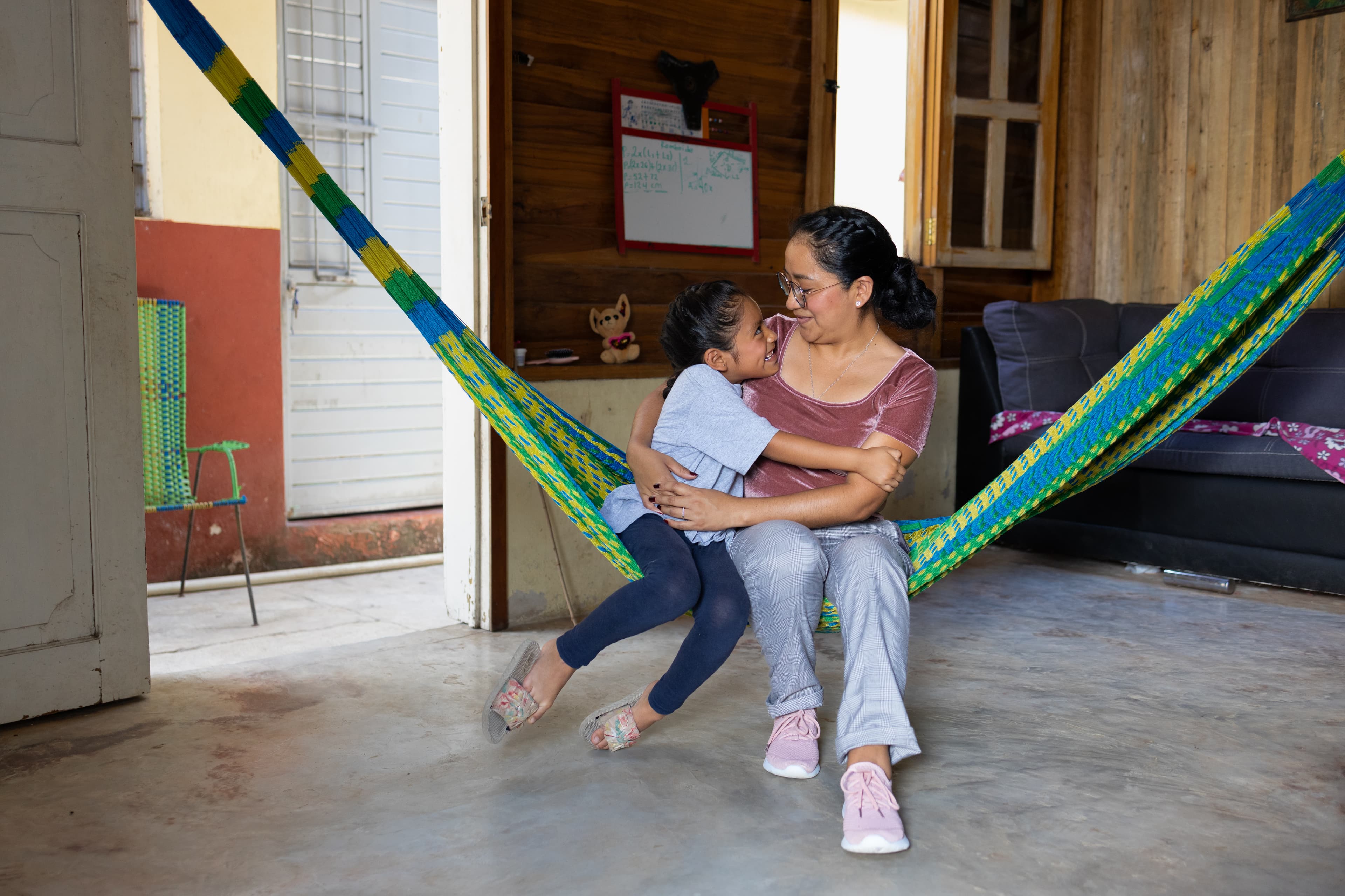 A young girl and her mother embrace while sitting on a hammock.