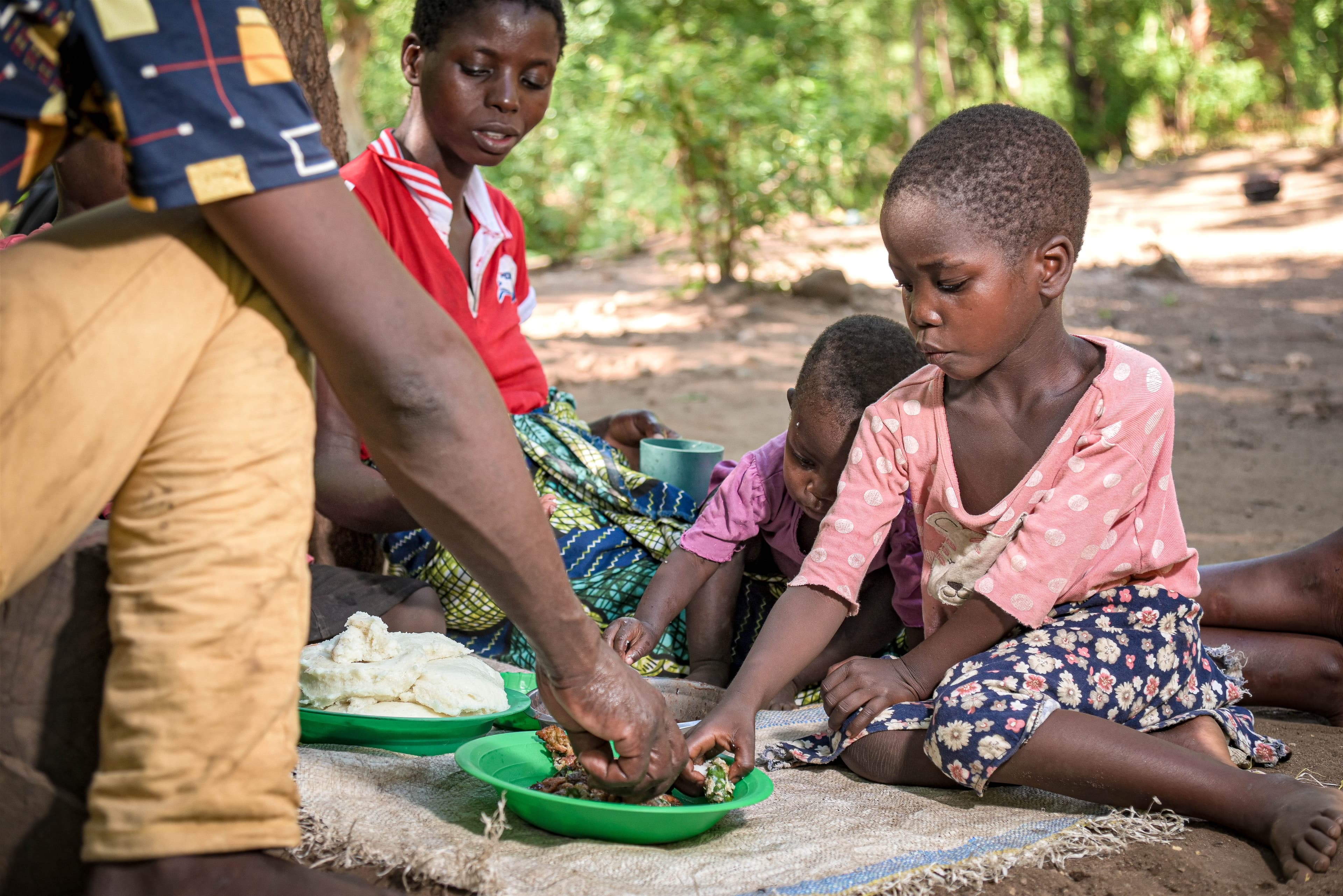 MW: More Than Just a MealA young African girl sits on the ground while eating from a green plate.