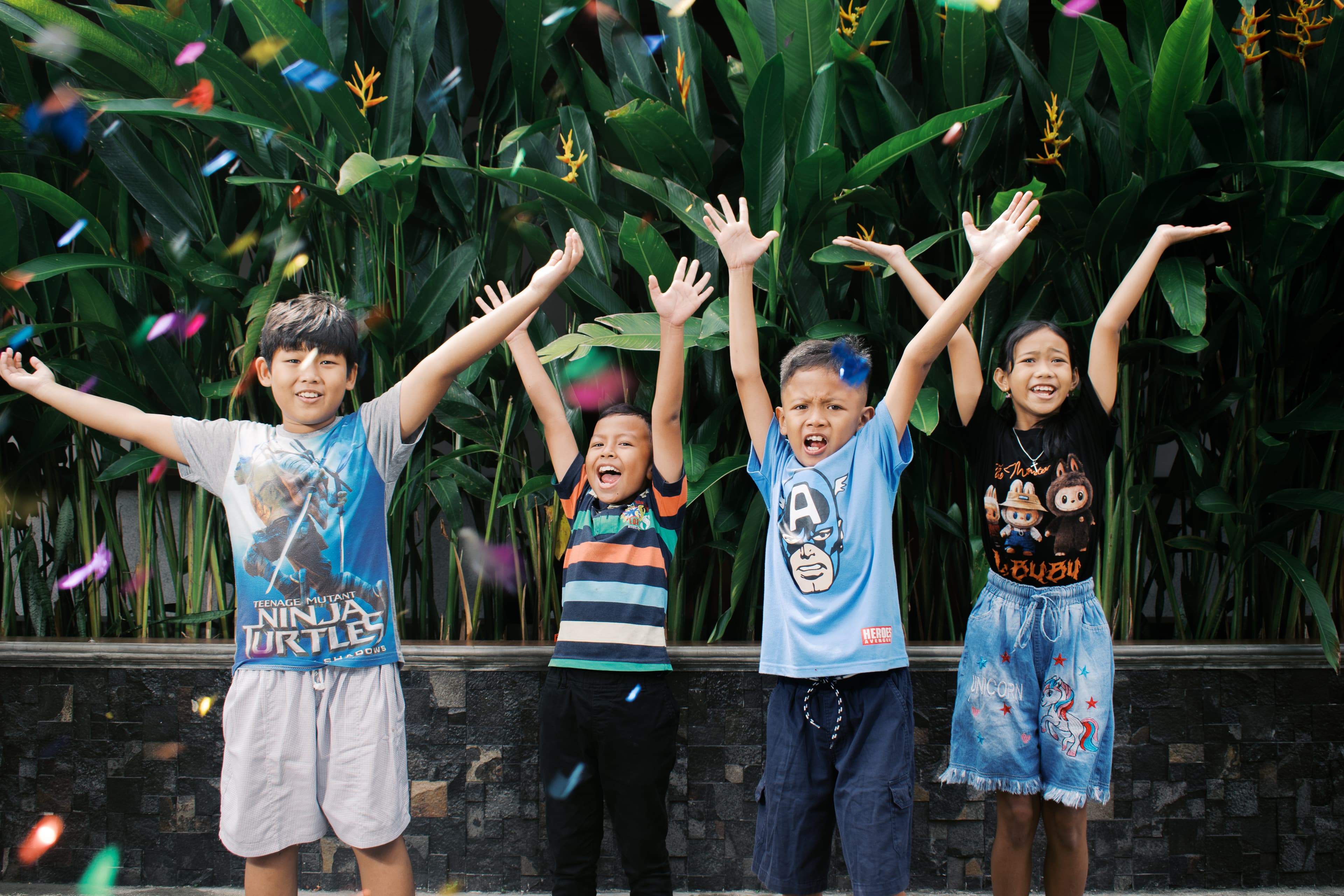 A group of children are smiling as they lift their hands in their air surrounded by bubbles.