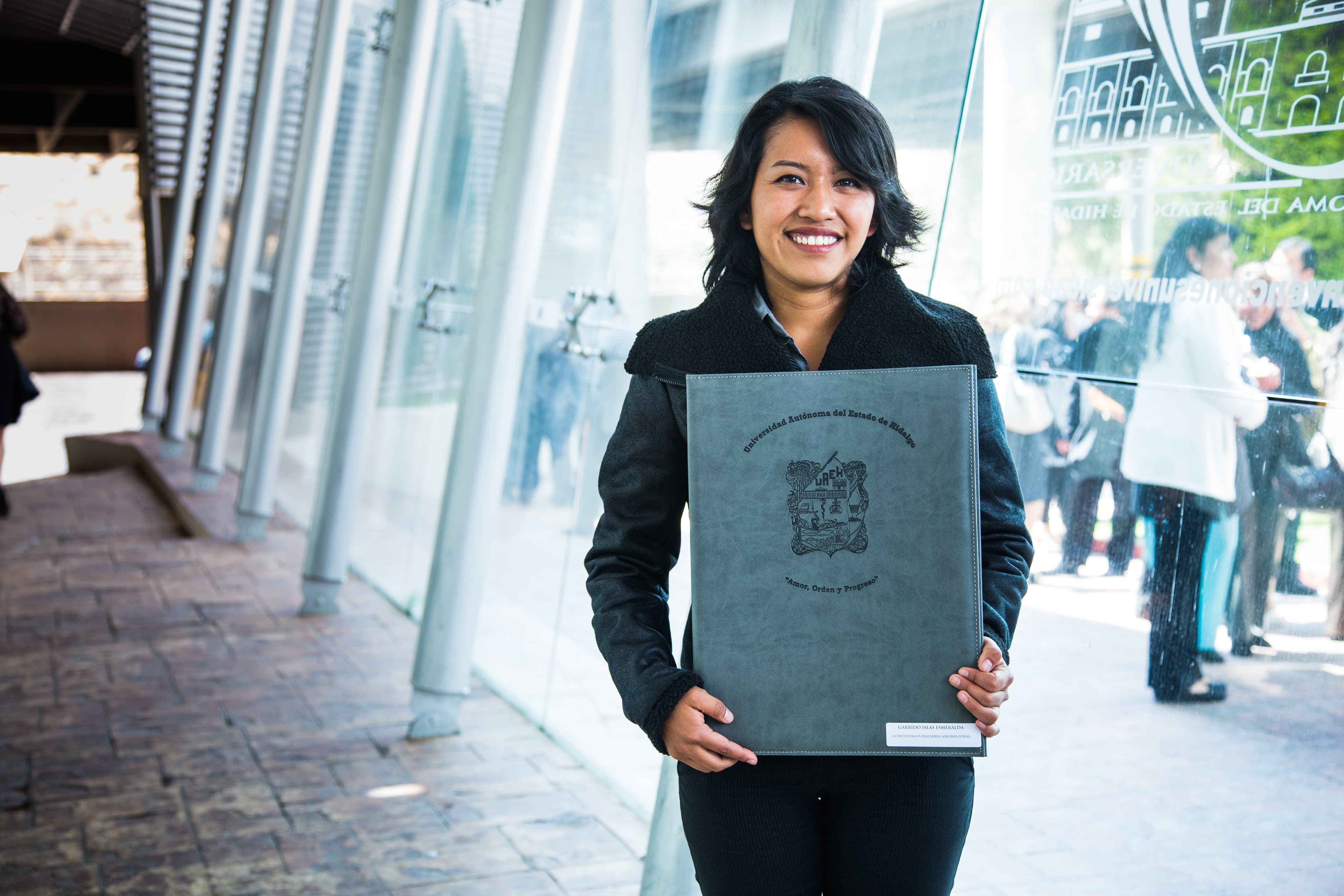 Young woman smiles as she holds her college diploma.