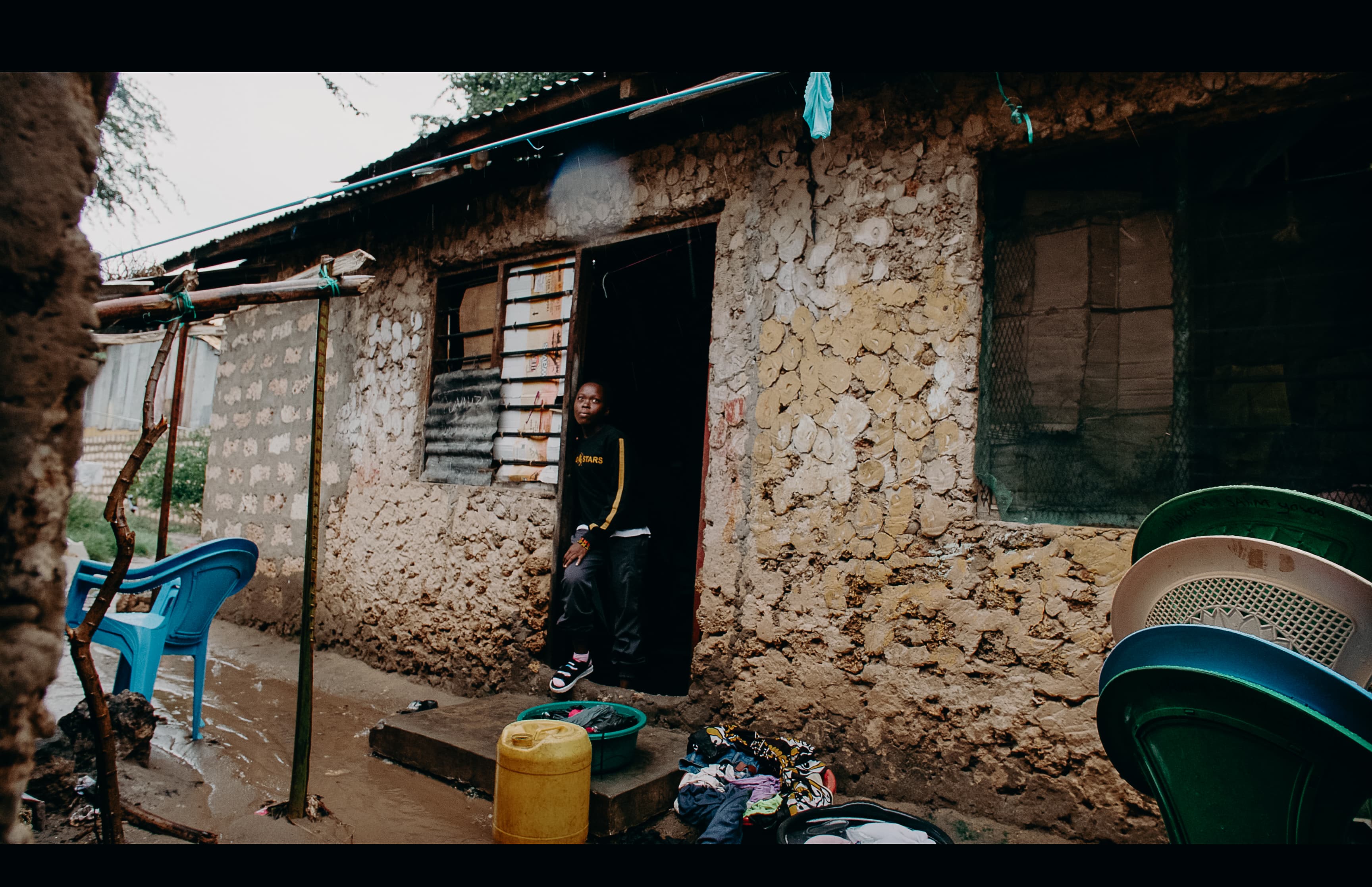 Kenyan woman wearing a black sweatshirt stands in the doorway of her home.