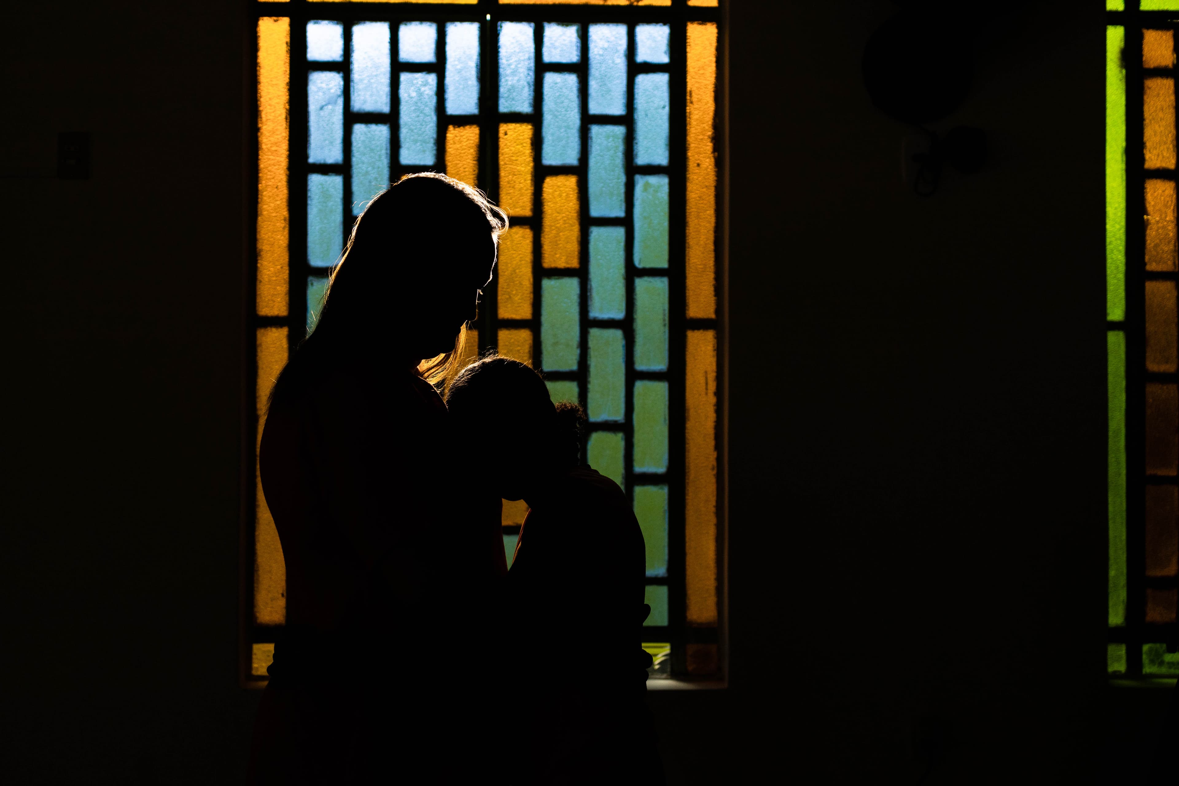 Silhouette of a woman and girl embracing in front of a stained glass window.