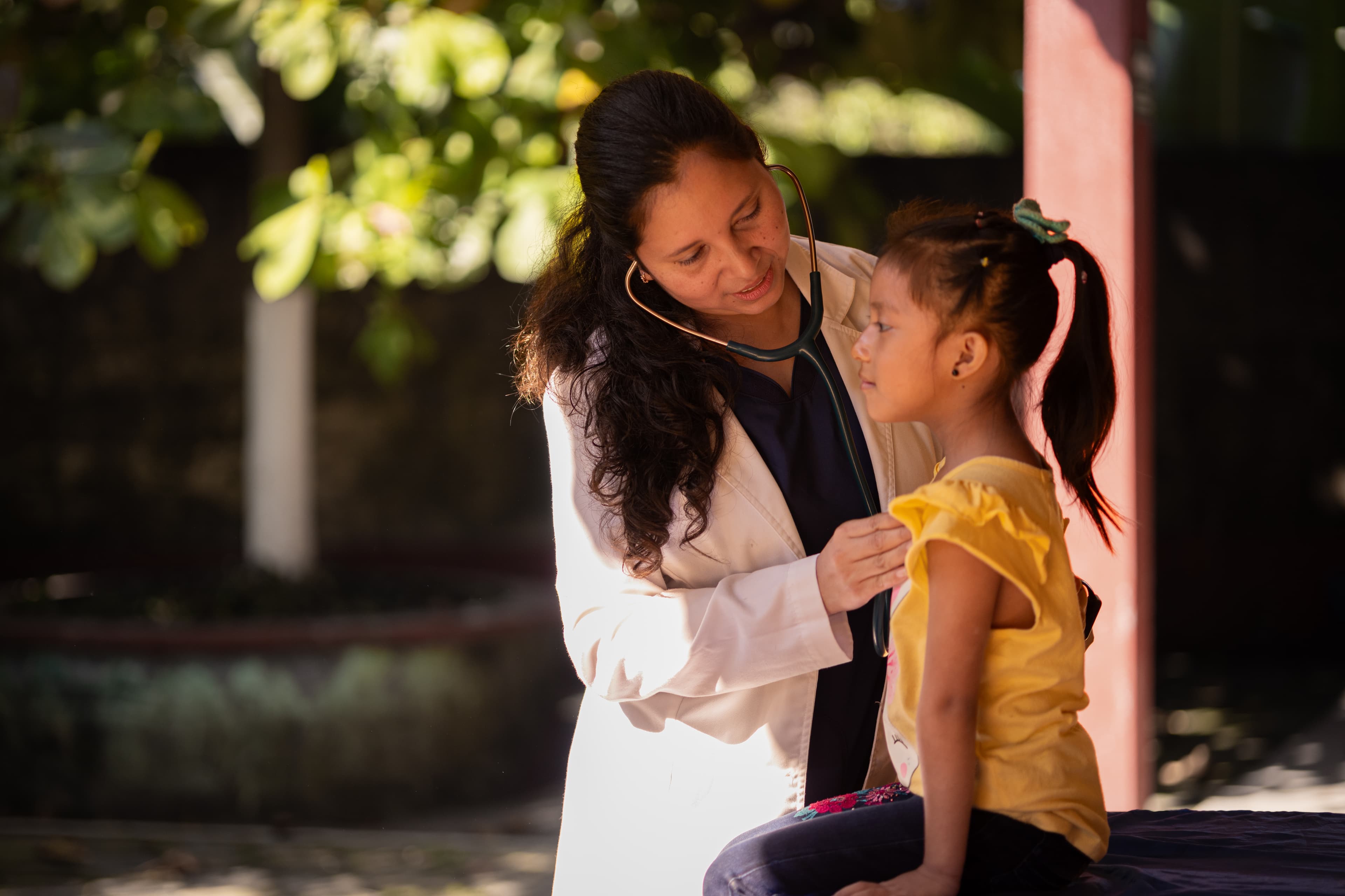 Female doctor examines young girl sitting outdoors