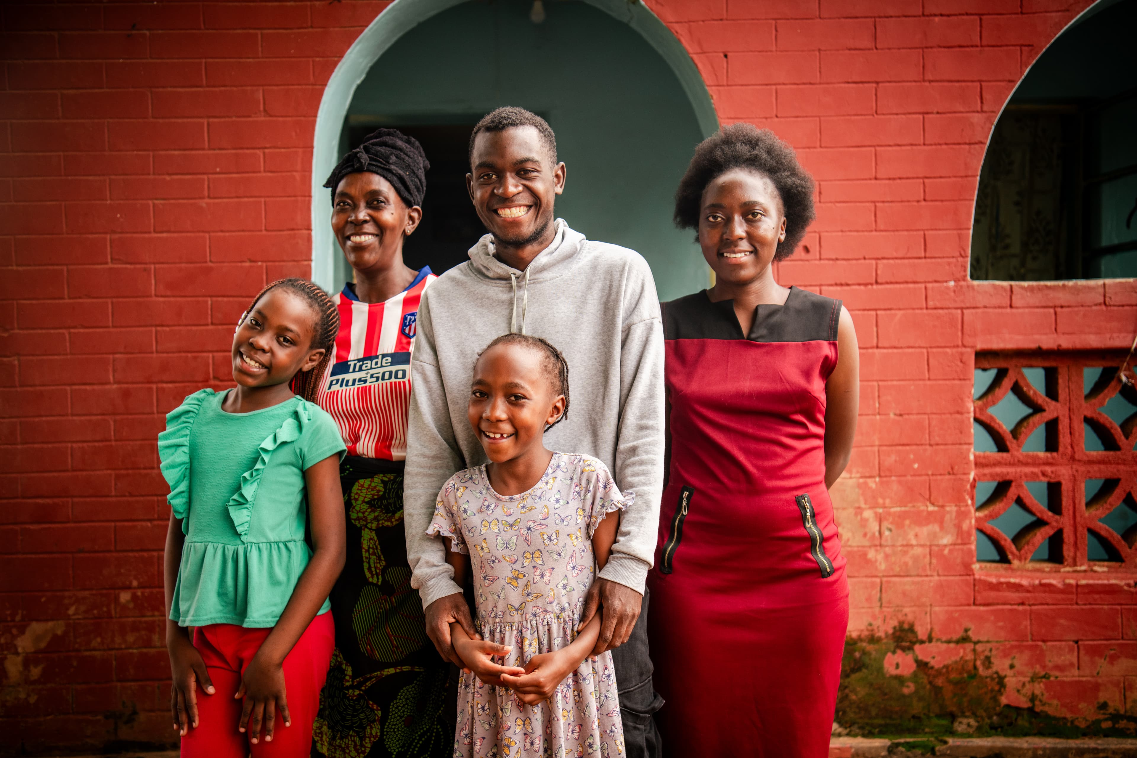 A man stands with his four family members for a portrait outside their brick home.