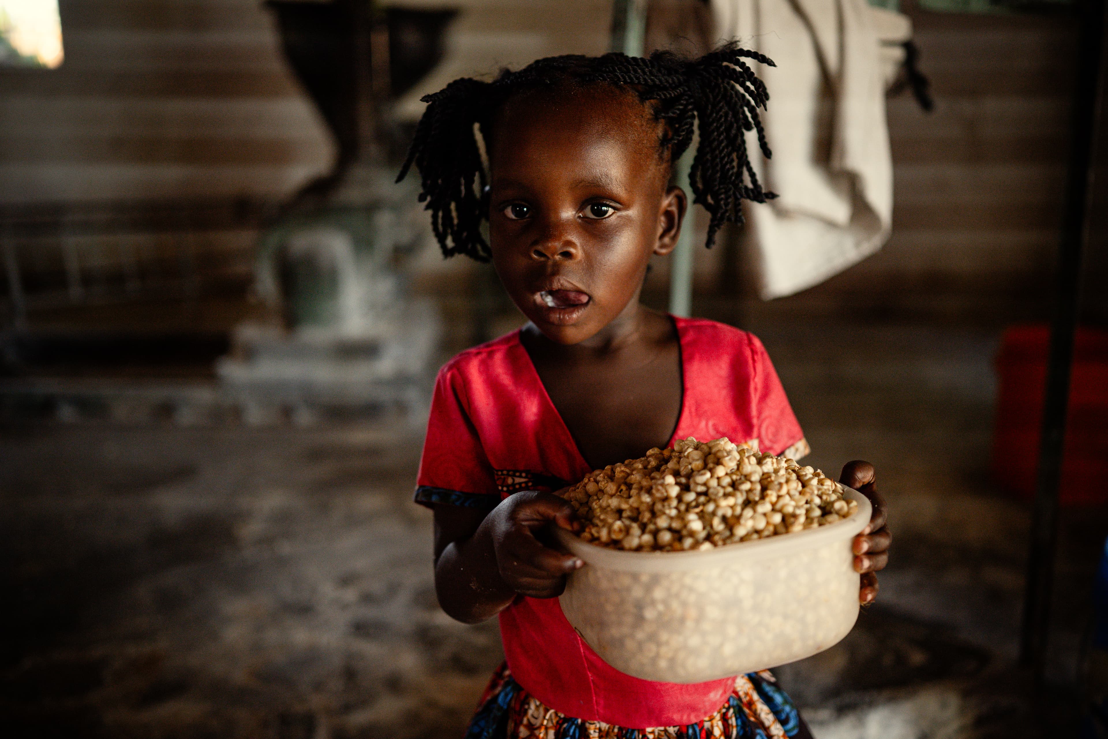 A young girl is holding a container of maize in her hands while looking at the camera.