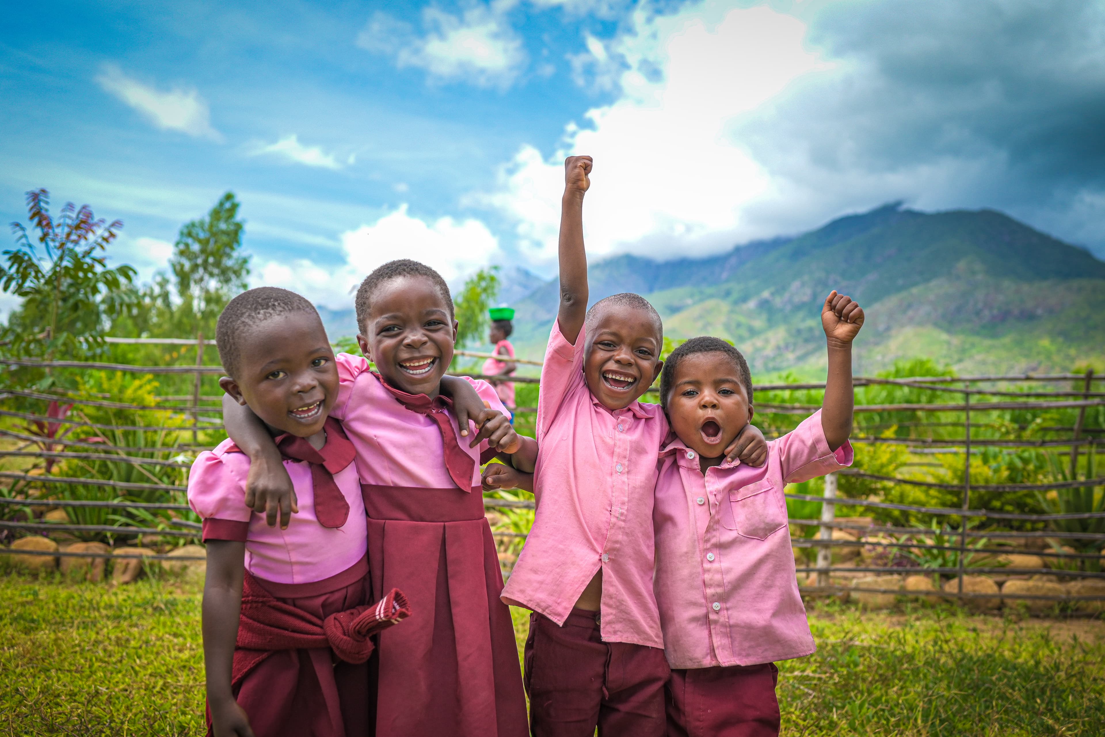 Four children wearing pink and burgundy school uniforms playfully pose for the camera.