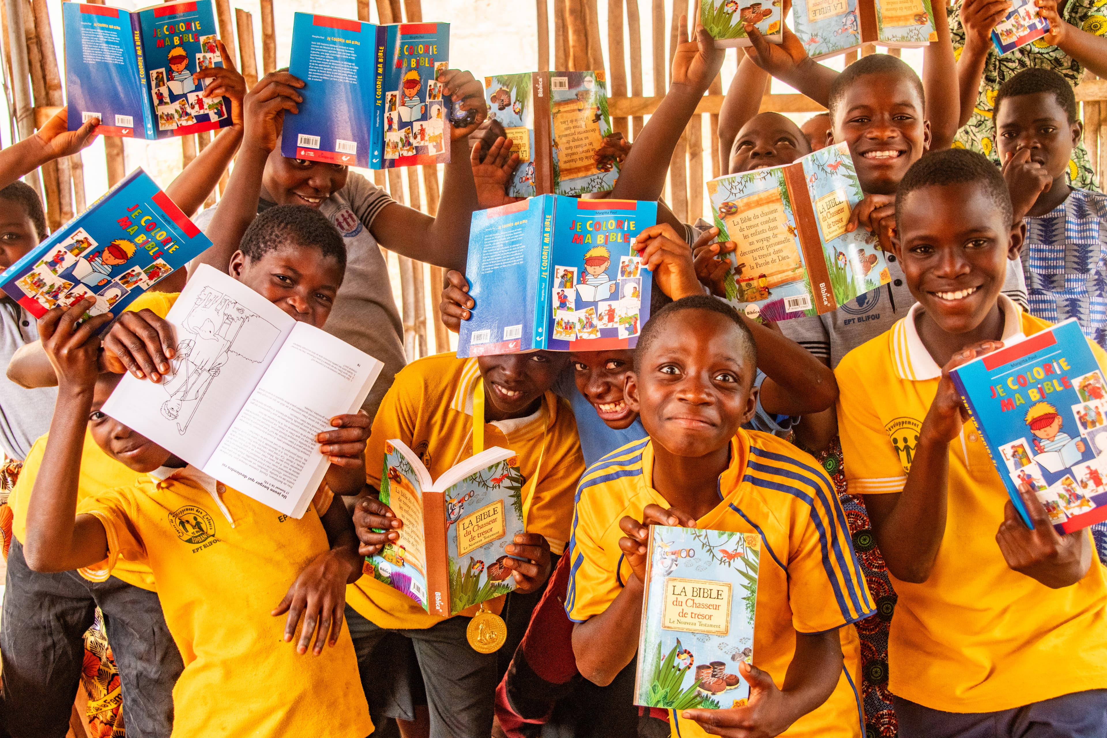 A group of children wearing yellow uniform shirts hold and show their Bibles, smiling.