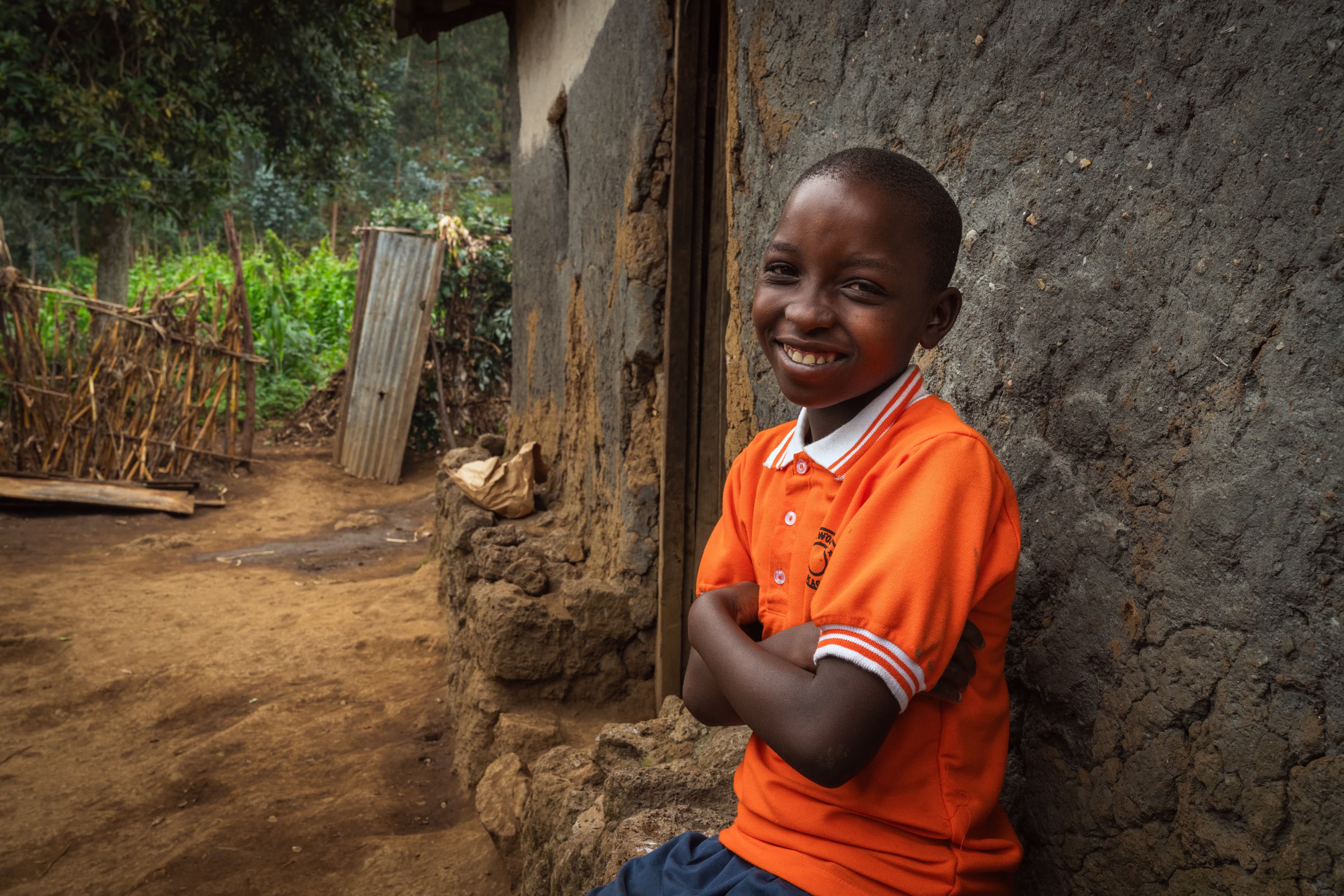 Young girl in orange polo shirt smiles with arms crossed while leaning on a stone wall