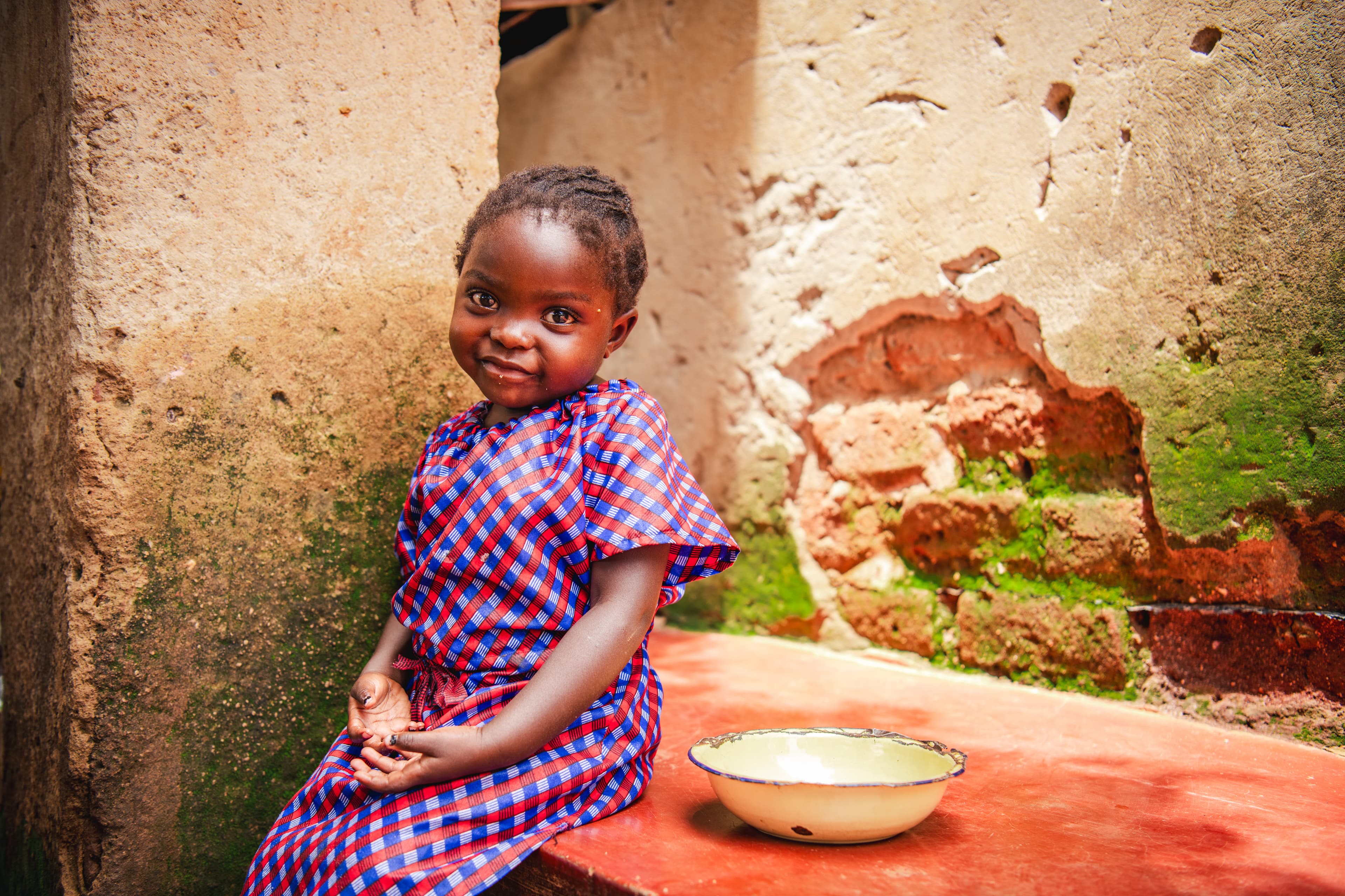 A little girl sits with her hands in her lap next to an empty bowl.