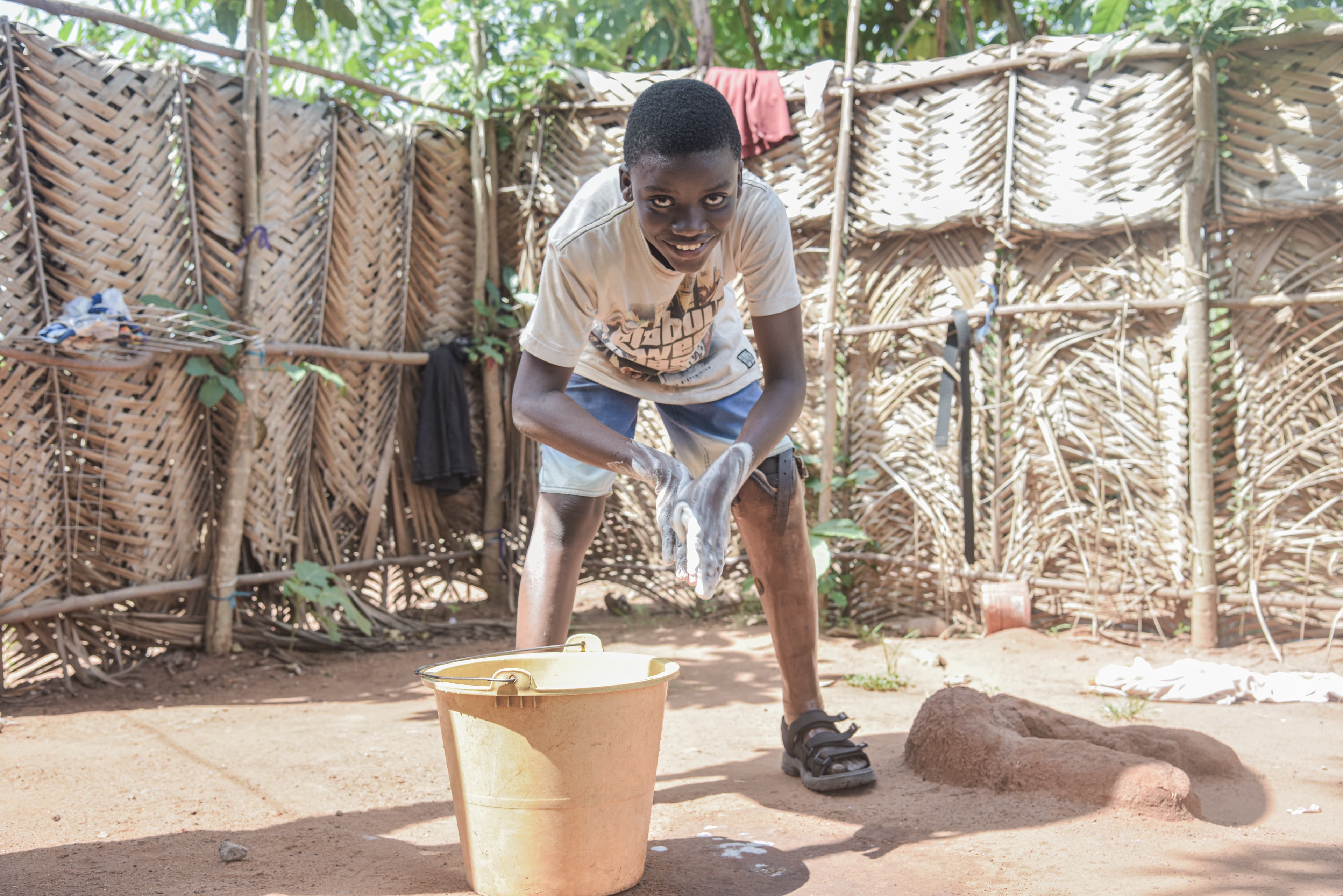 A young boy stands and smiles while washing his hands.