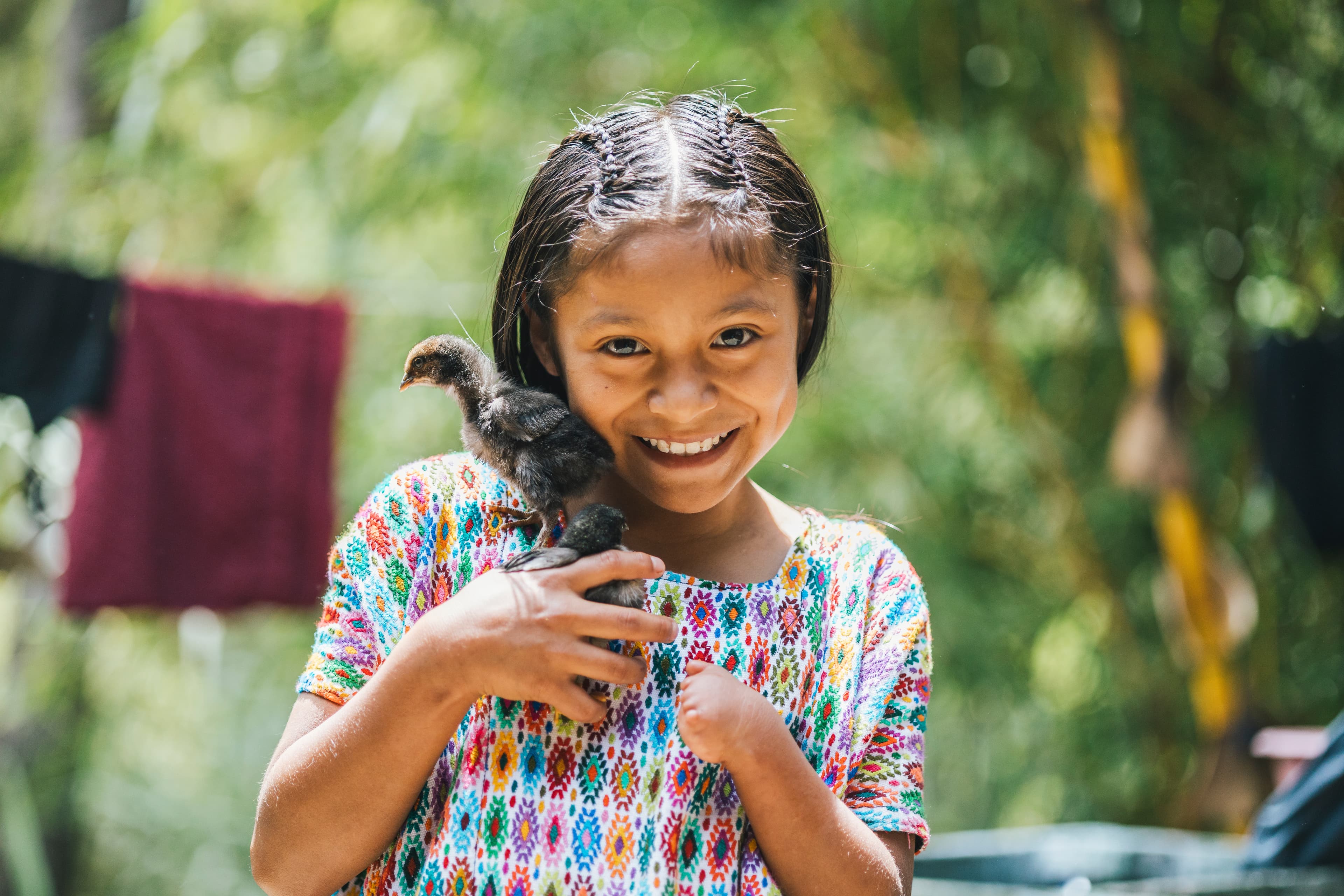 Smiling portrait of a young girl standing in her backyard holding a couple of baby chicks.