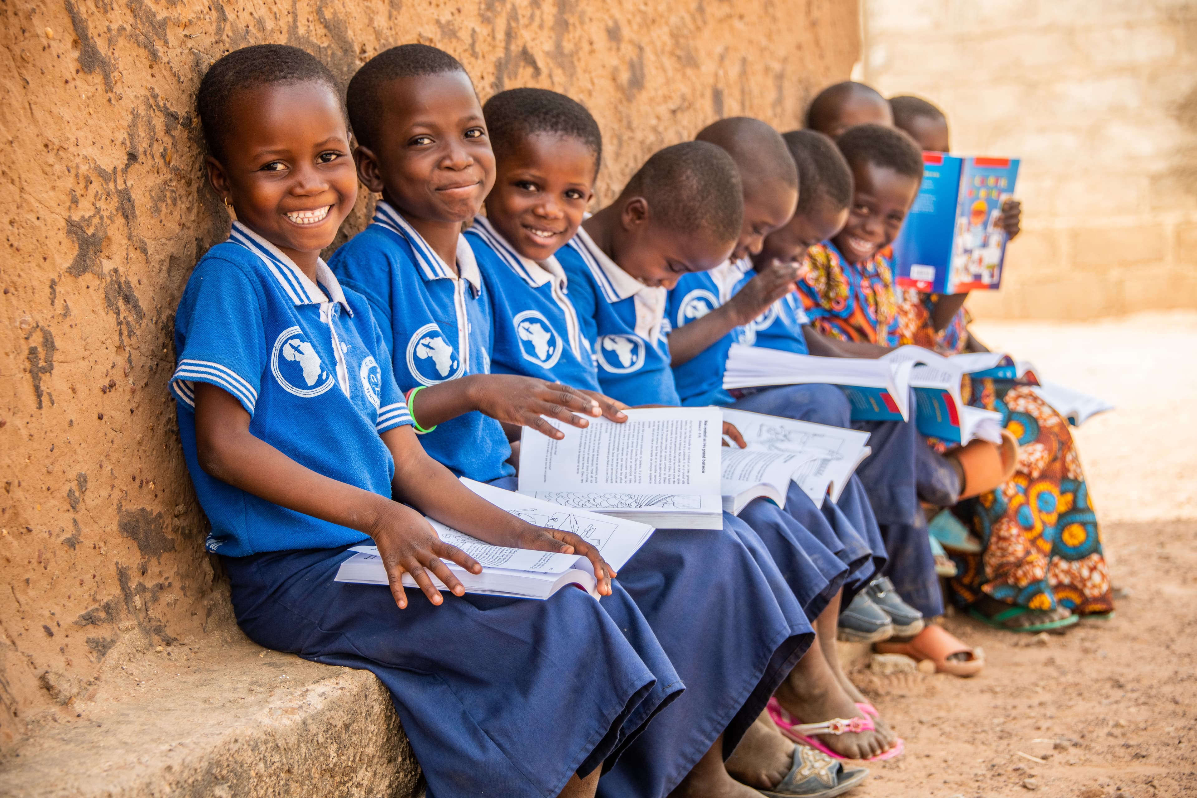 A group of young girls are smiling and sitting with bibles open in their laps.