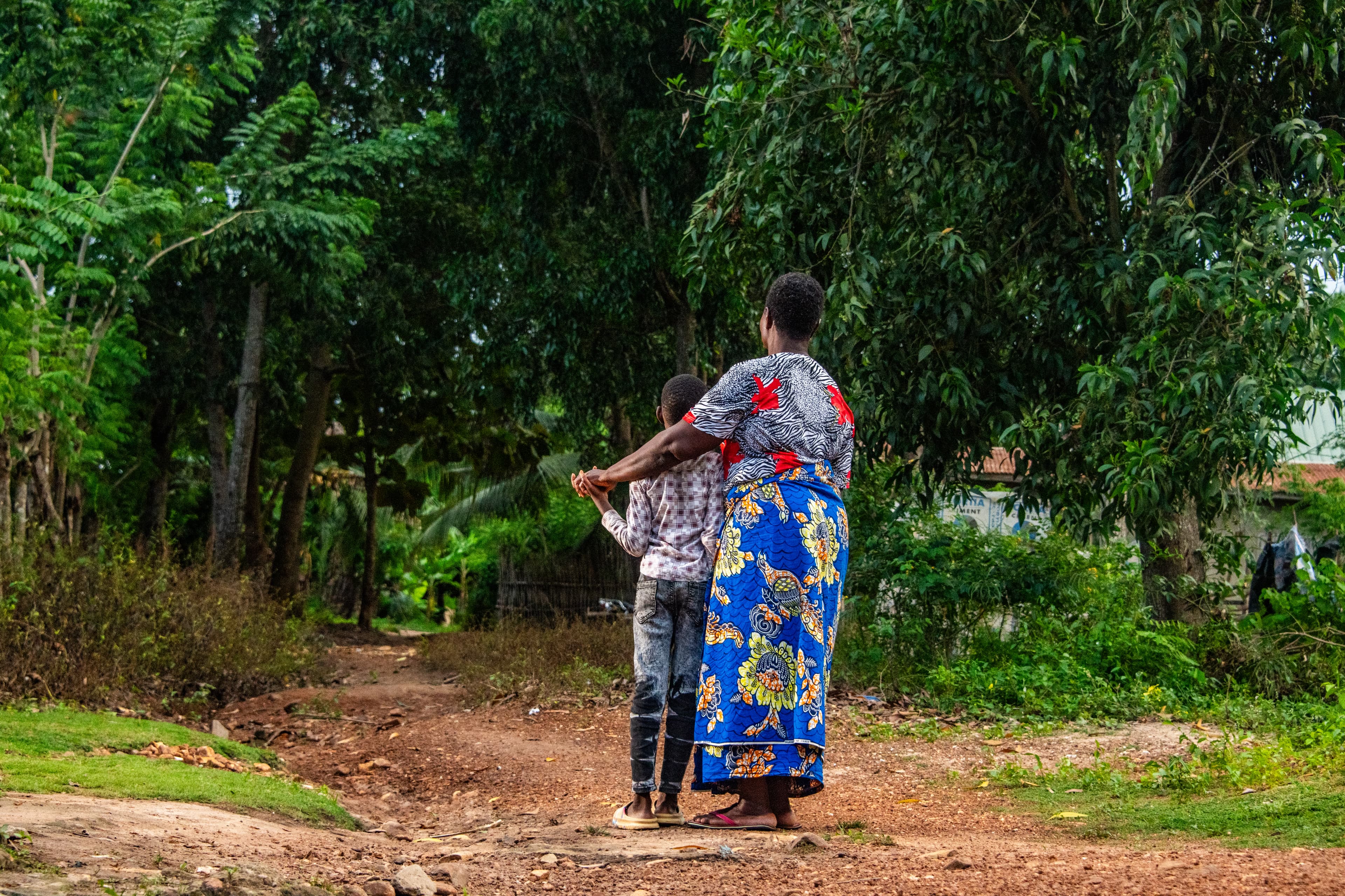 An older woman and a young boy hold hands on a dirt road with their backs to the camera.
