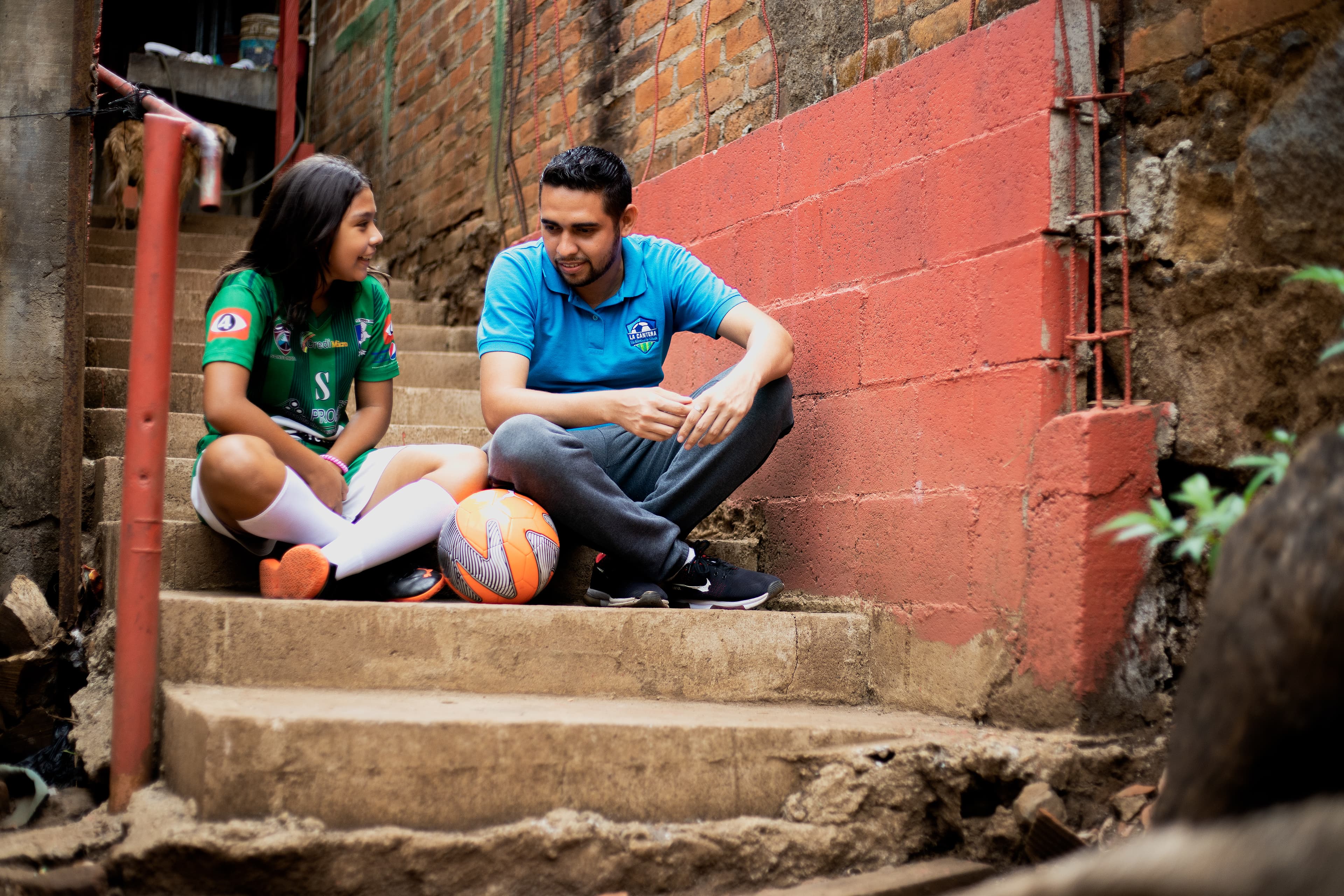 A young girl and an older man sit on concrete steps with a soccer ball.