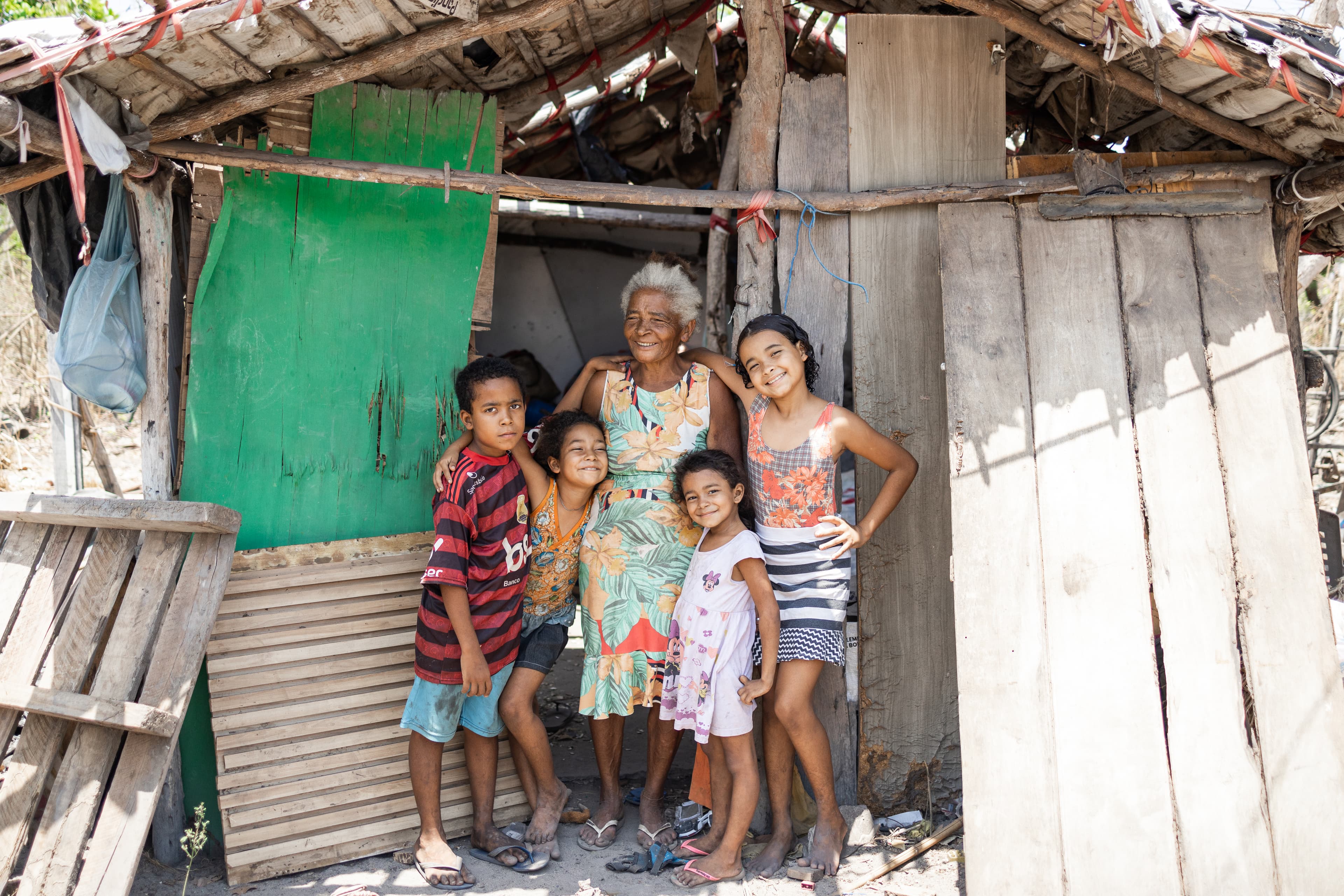 An elderly woman and four children stand outside a home while smiling.